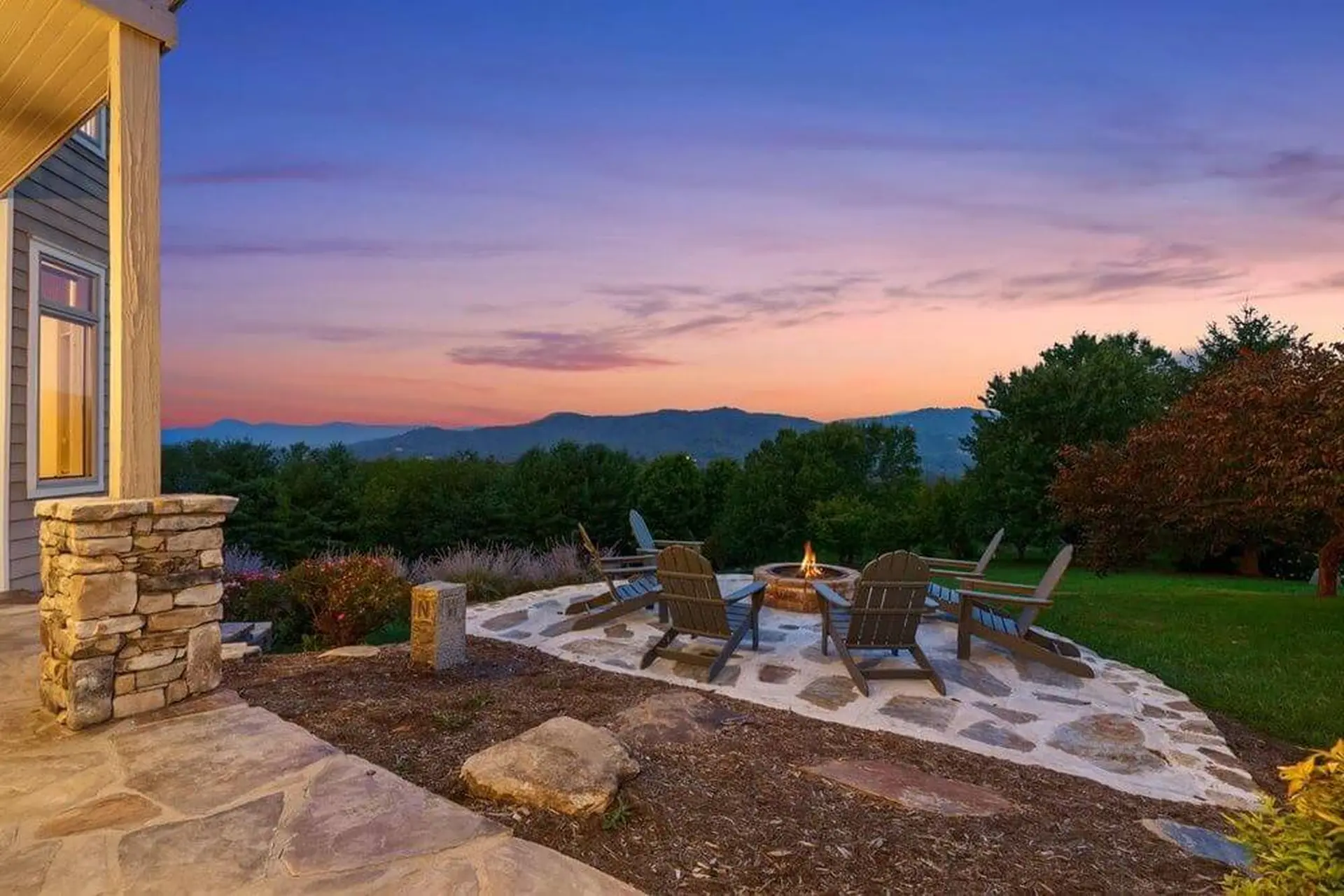 Patio with a fire pit and chairs overlooks mountains at sunset.