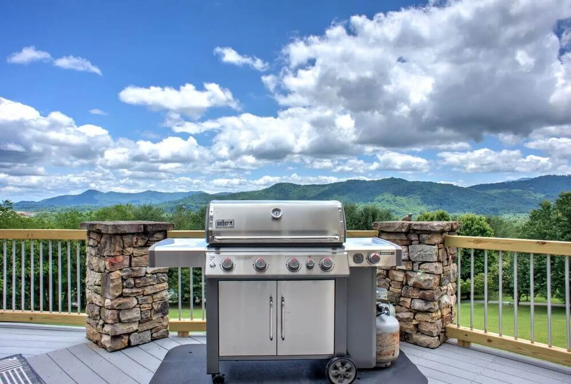 A stainless steel grill sits on a deck with a mountain view.