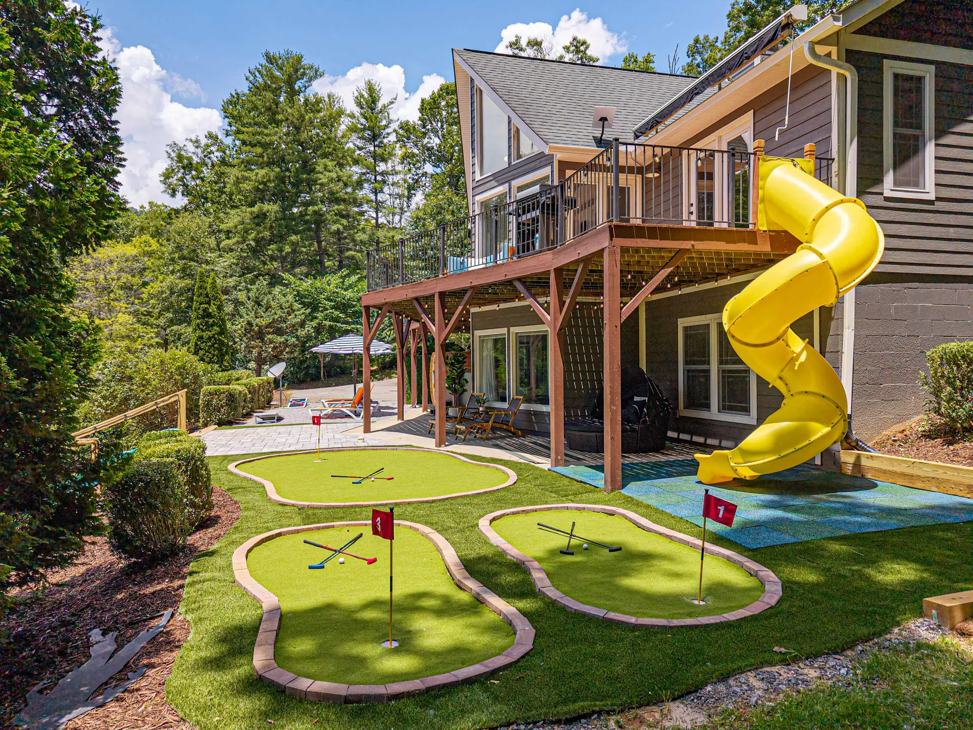 Backyard with a yellow tube slide, mini golf course, and patio area.