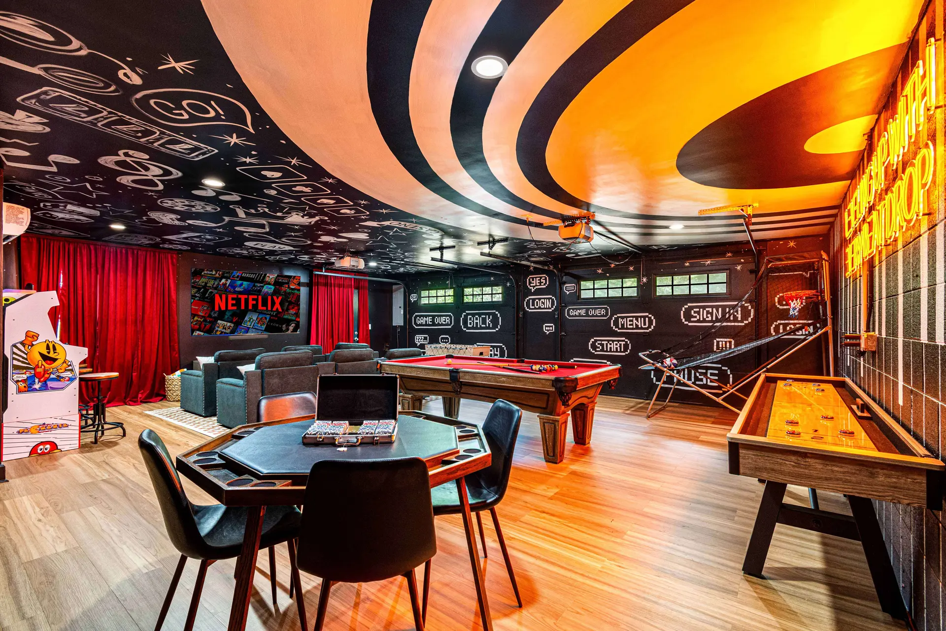 A game room with a pool table, shuffleboard, Pac-Man arcade machine, and a Netflix screen on the wal