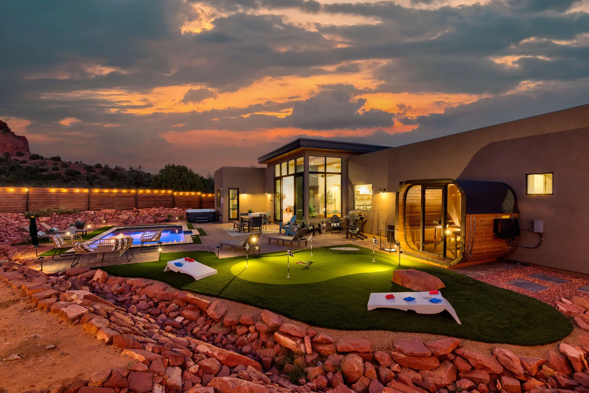 Luxury outdoor living with pool, hot tub, putting green, and sauna at sunset.