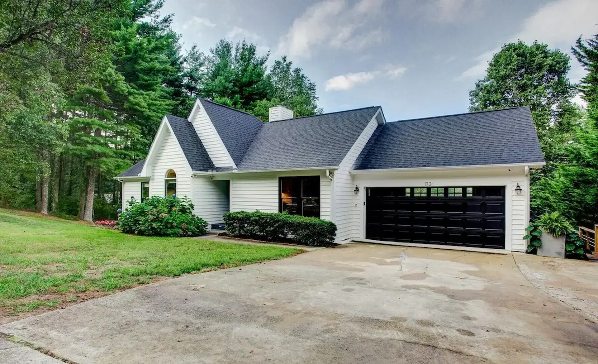 A white house with a black garage door is surrounded by trees.