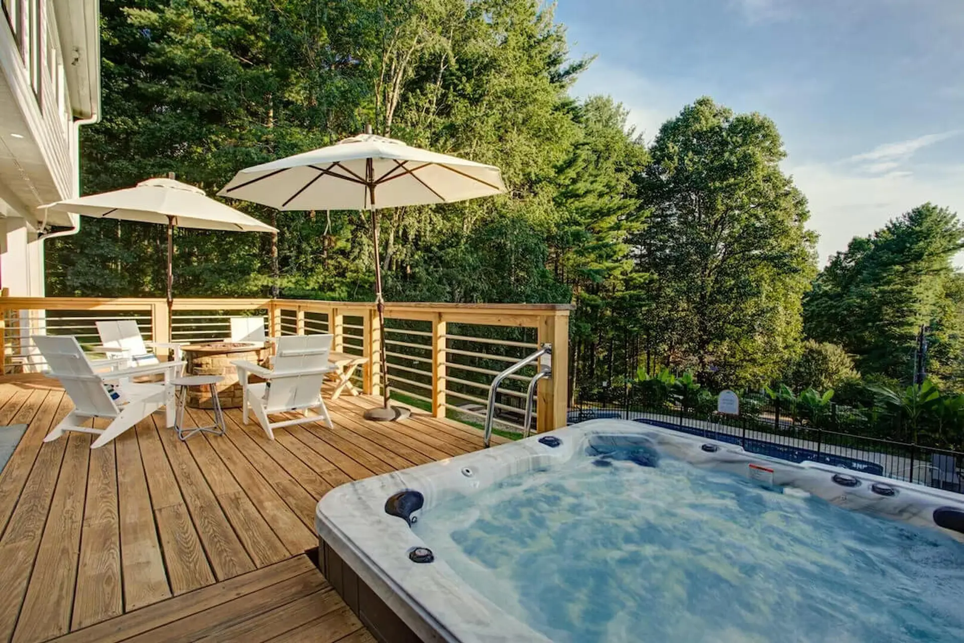 Outdoor deck with a hot tub, white chairs, umbrellas, and a fire pit.