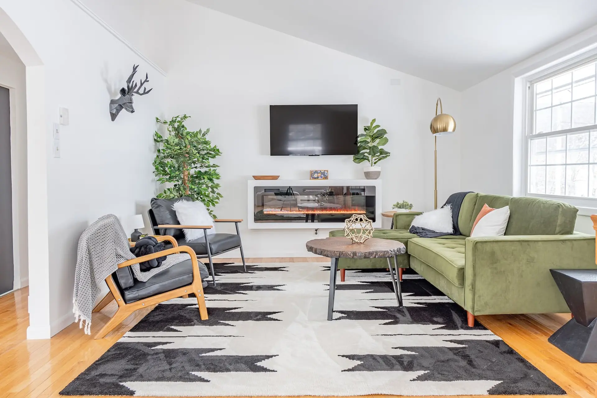 Modern living room with a green velvet sectional, geometric rug, and fireplace.