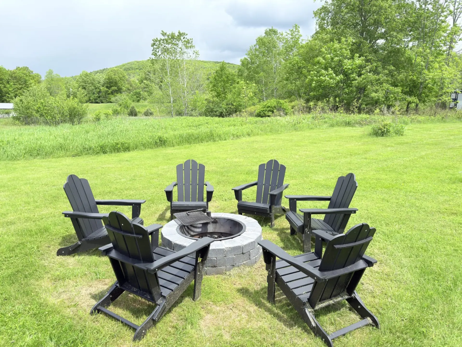 Black Adirondack chairs are arranged in a circle around a fire pit in a grassy yard.