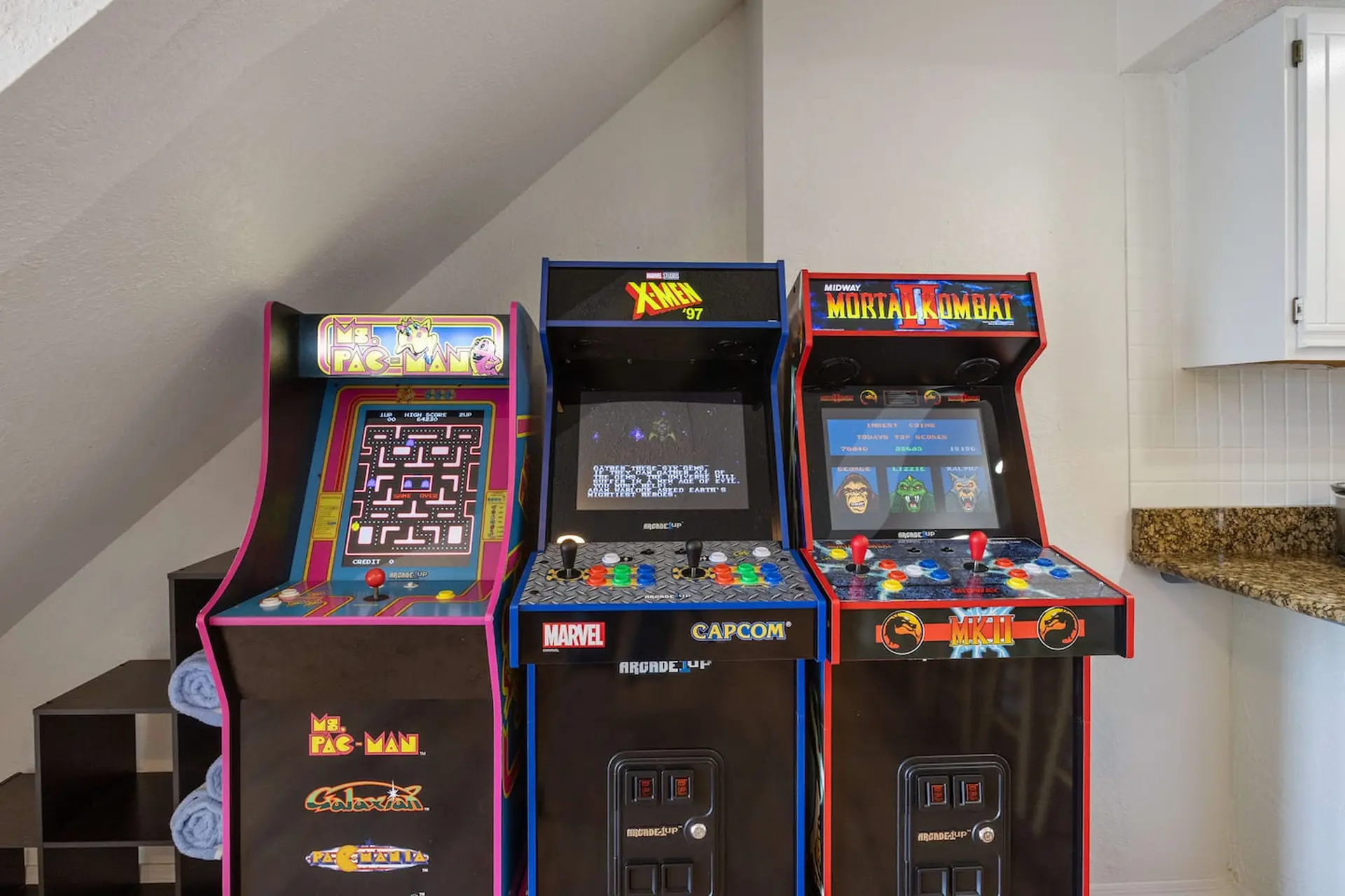 Three arcade cabinets: Ms. Pac-Man, X-Men '97, and Mortal Kombat.