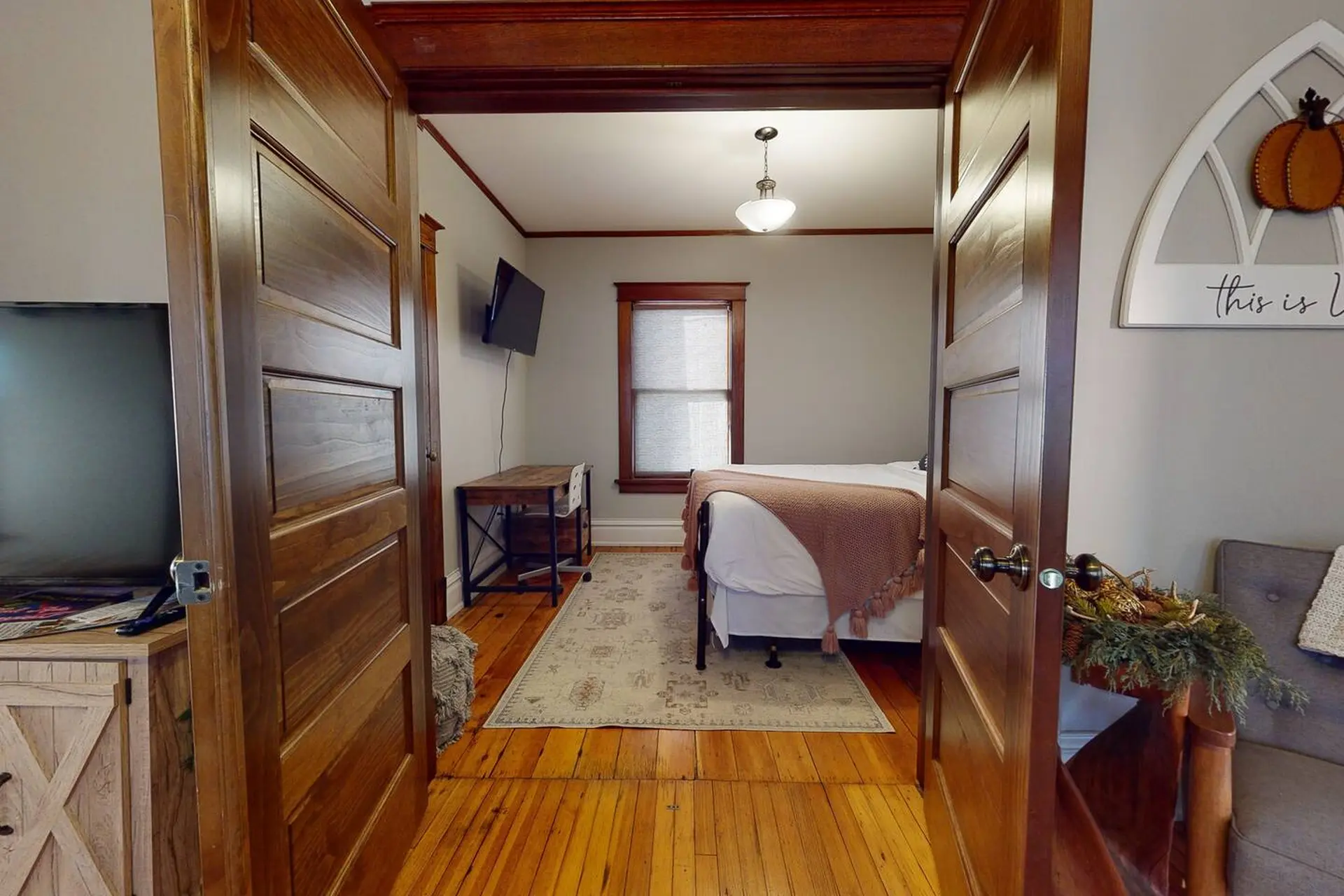 A bedroom features a bed, desk, and TV. Wood doors are open.