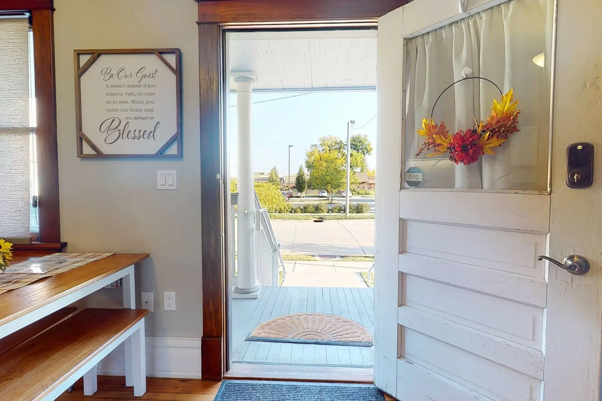 An open front door reveals a view of a porch, yard, and street.