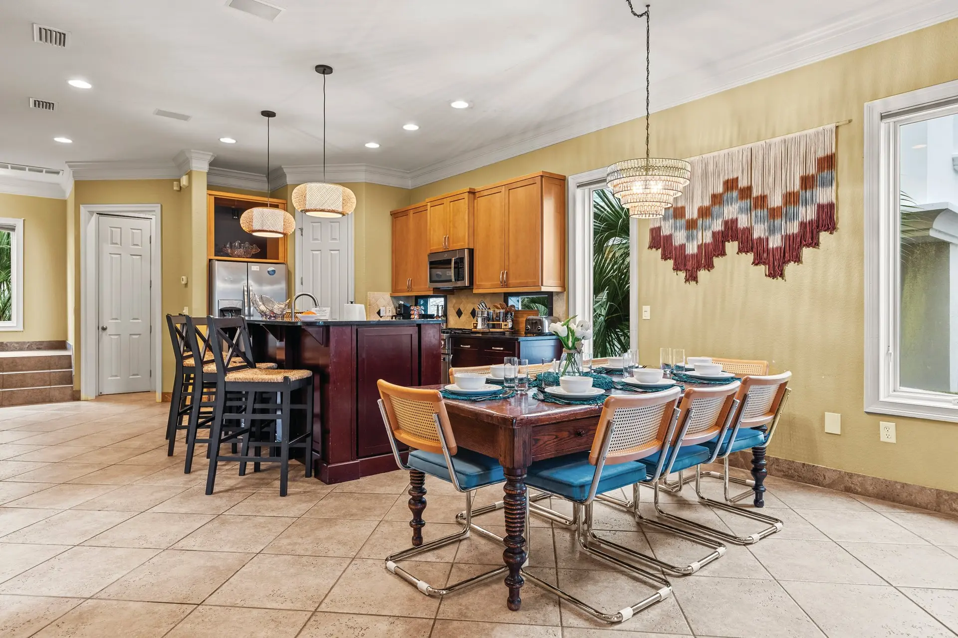 A dining set and kitchen island are in a room with beige walls and tiled floor.