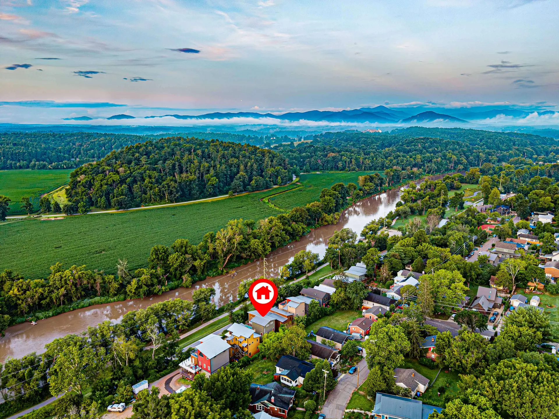 An aerial view of a neighborhood beside a river, with a red house marker in the center.