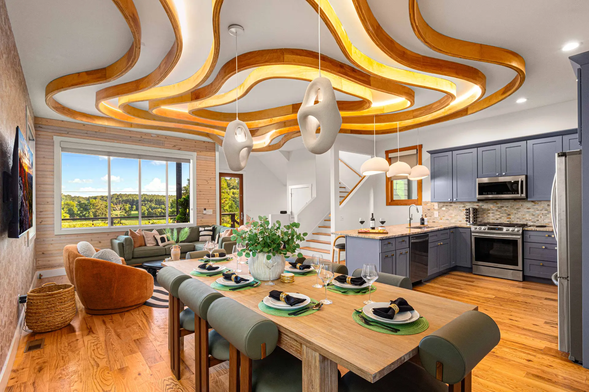 A spacious dining room features a light wood table set for a meal, with a modern kitchen and living 