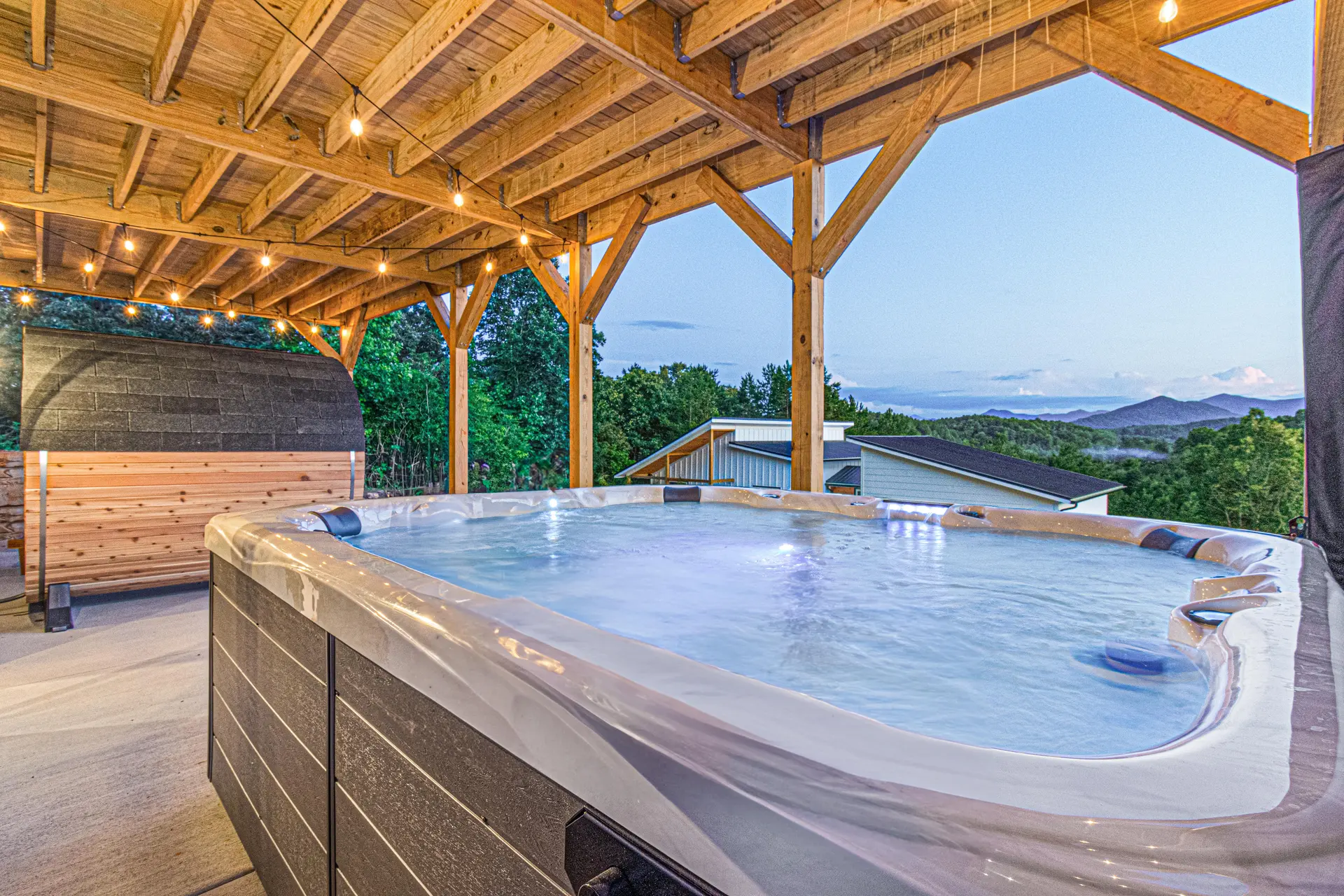Outdoor hot tub with a covered wooden deck, string lights, and a mountain view.
