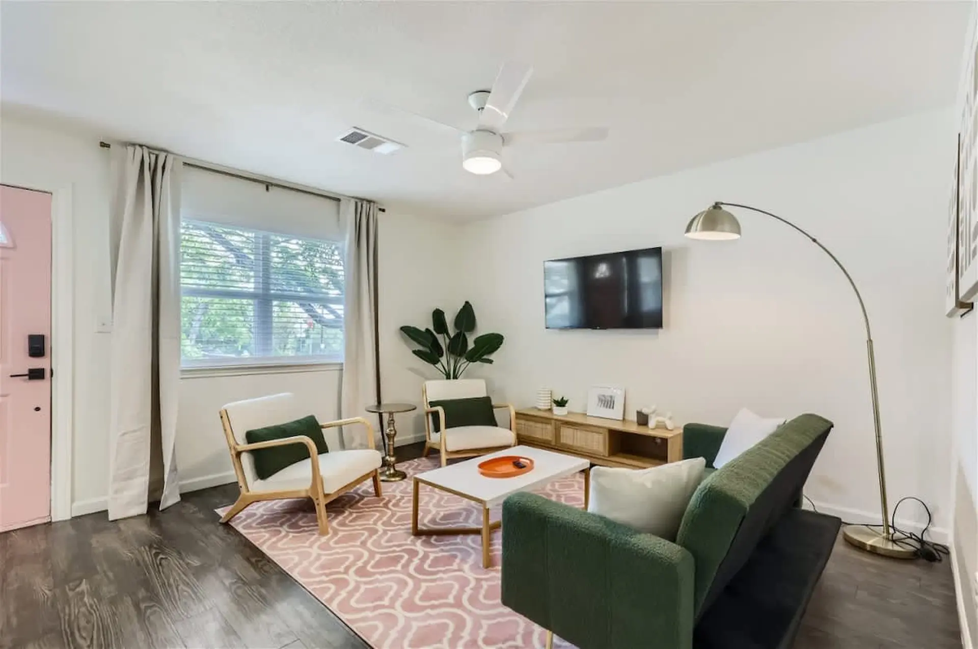 A stylish living room with a green sofa, chairs, coffee table, TV, and a floor lamp.