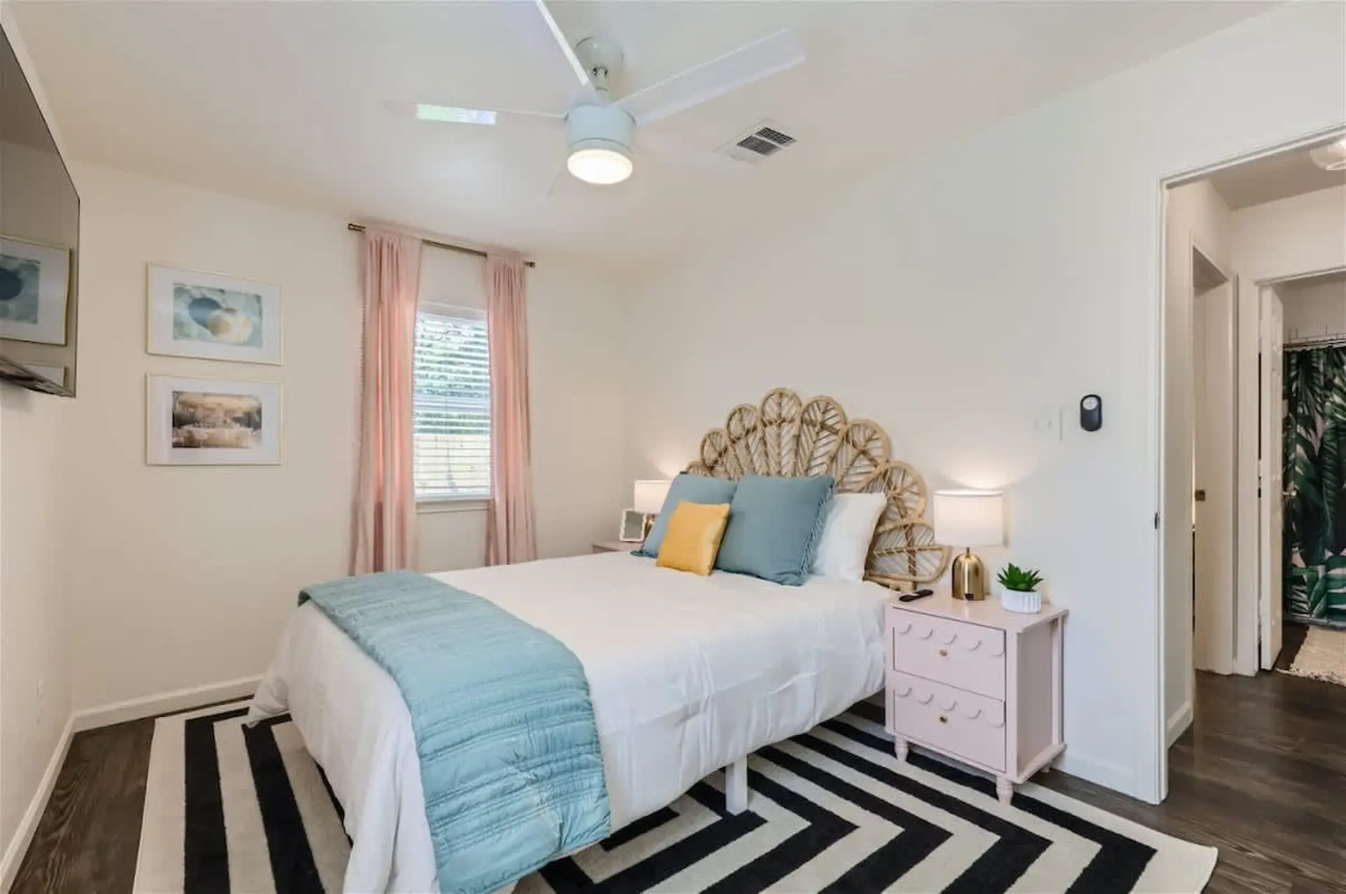 A bedroom with a queen bed, wicker headboard, and pink nightstand.