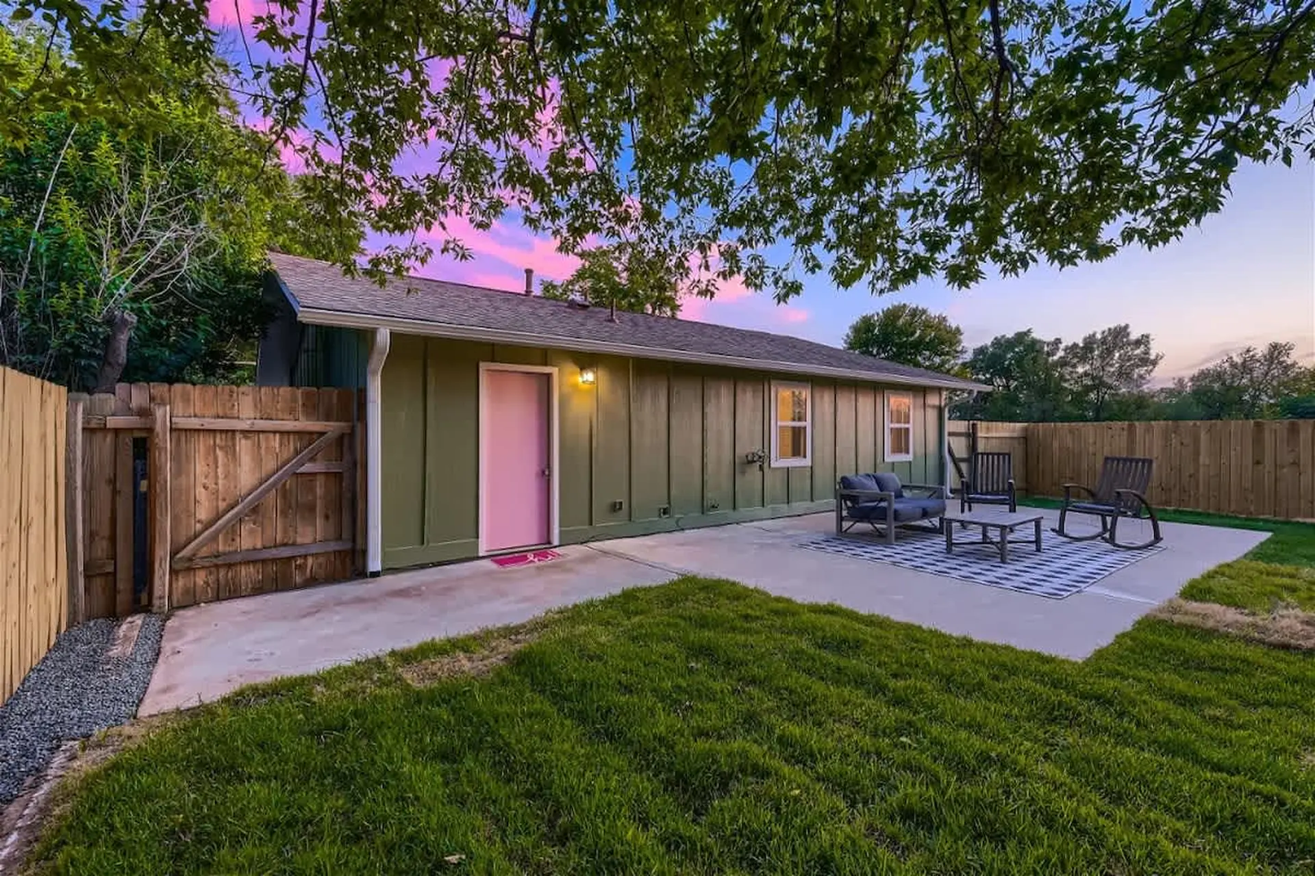 A green house with a pink door and a patio with outdoor furniture.