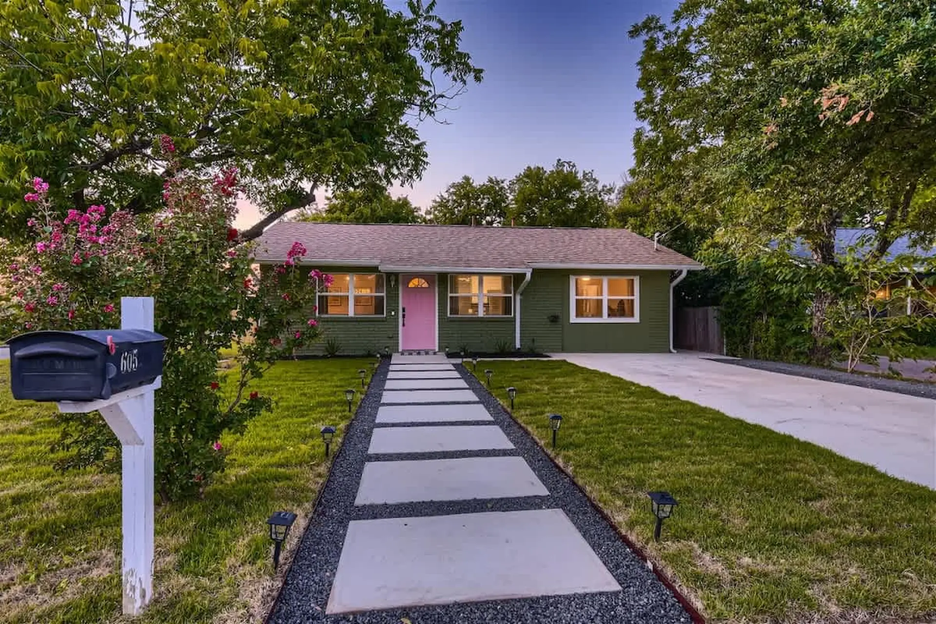 A green house with a pink door and a stone walkway.