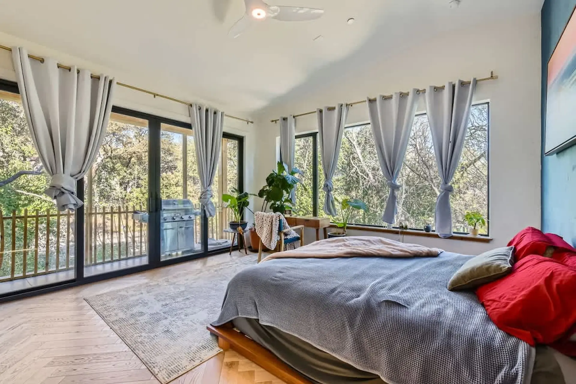 A bedroom with a bed, plants, and a grill visible through the window.