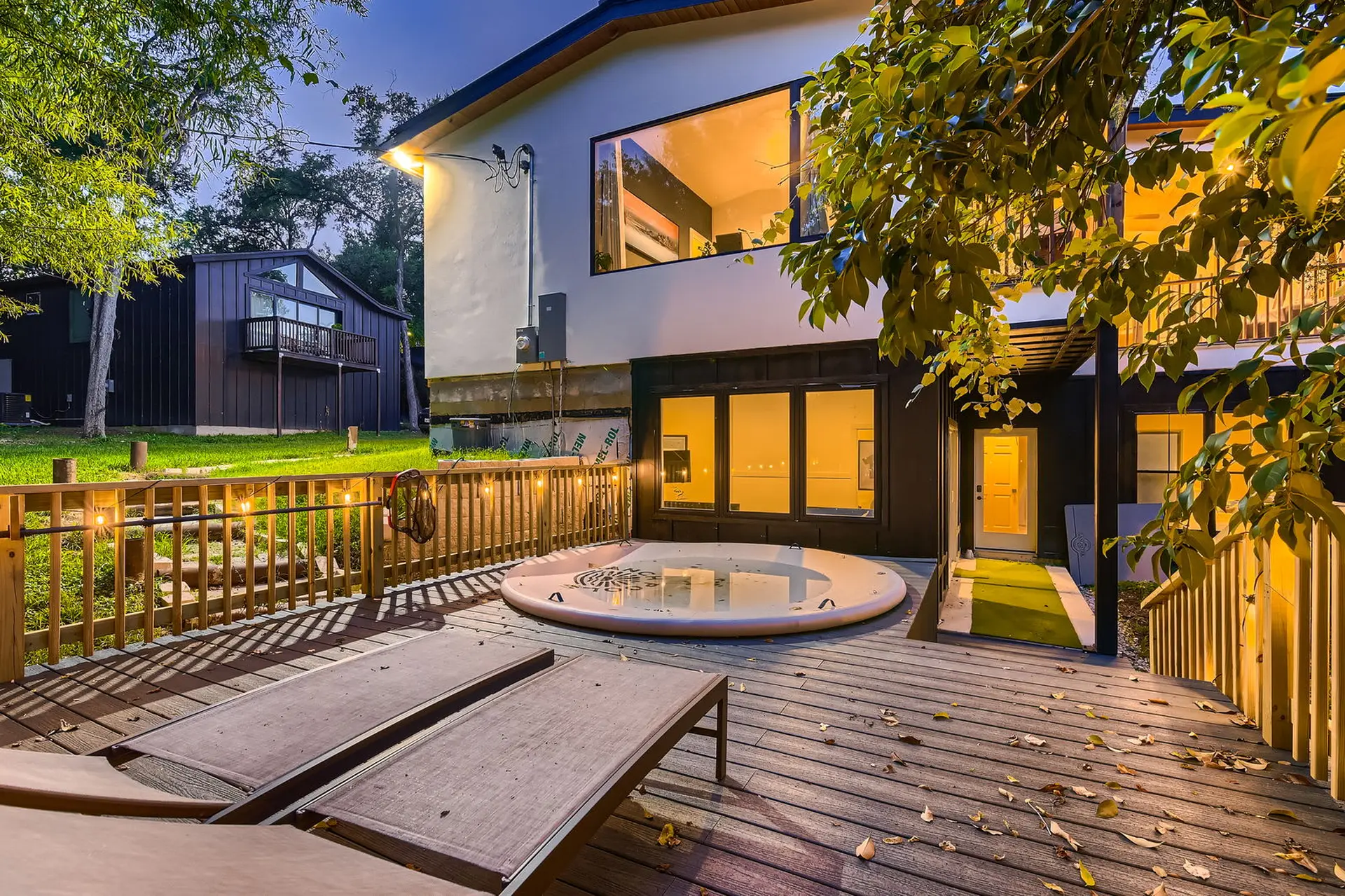 Modern home deck with hot tub, lounge chairs, and string lights at twilight.