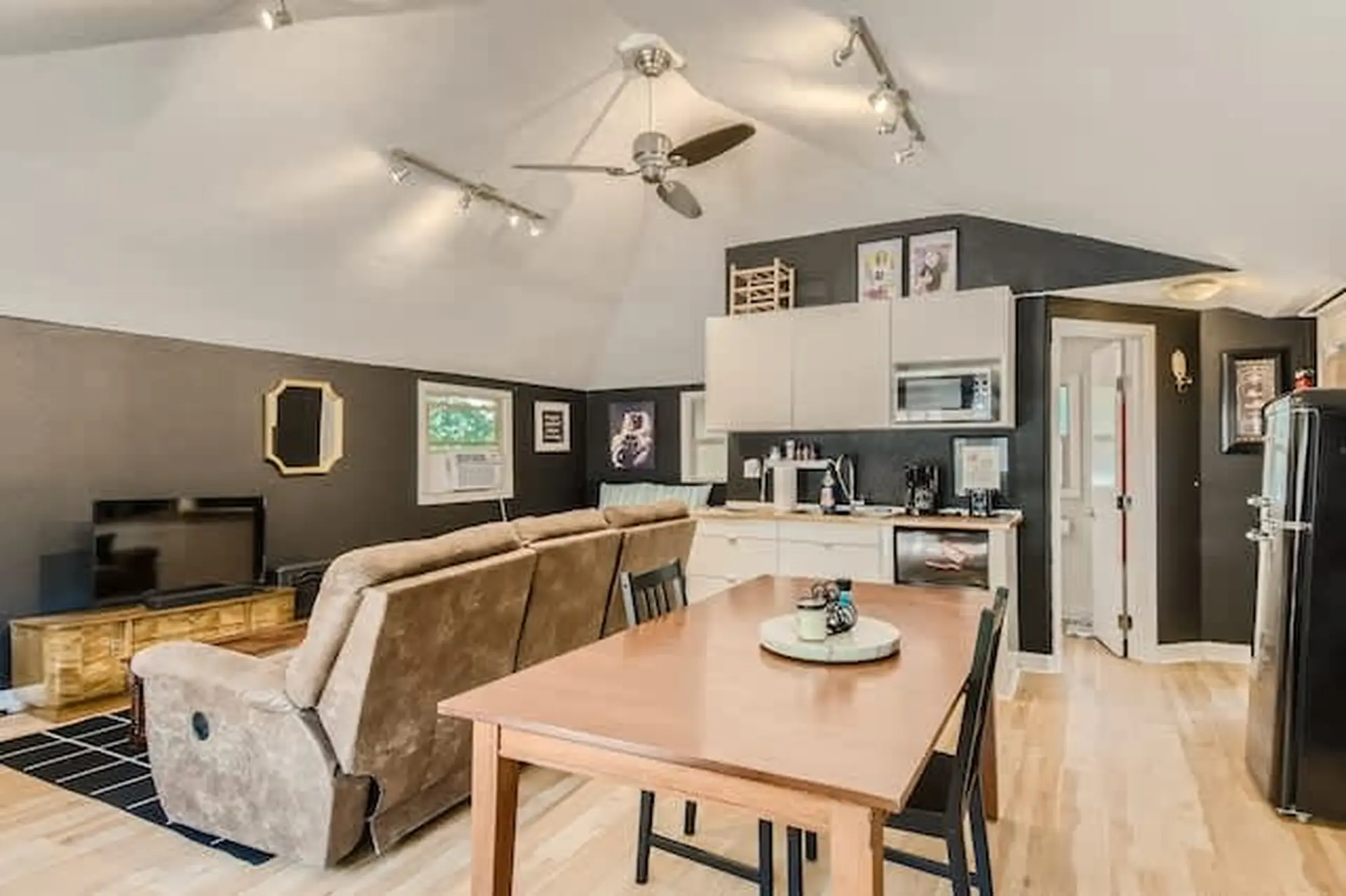 A ceiling fan hangs above a couch and dining table in a cozy living room and kitchen area.