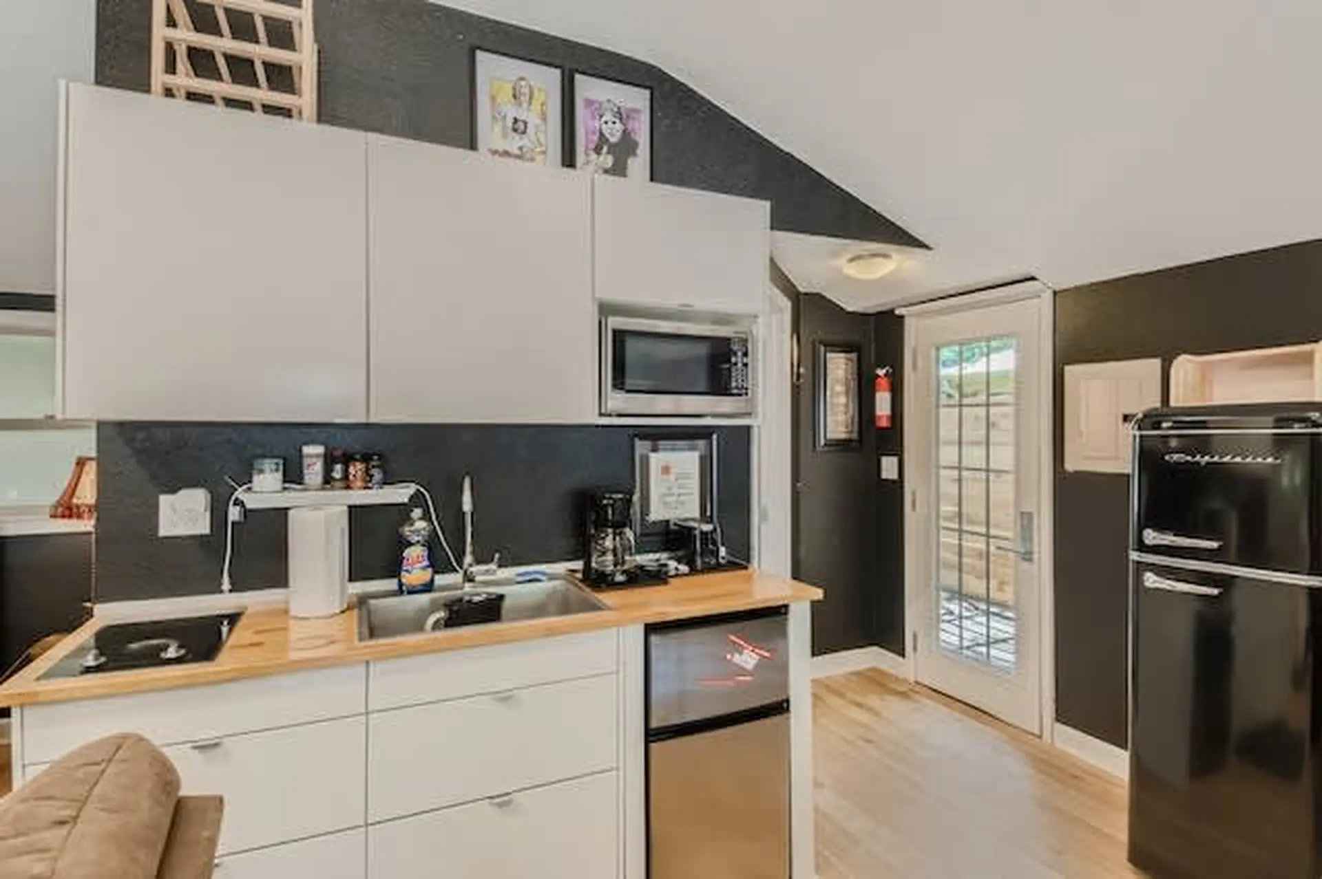A small kitchen with white cabinets, a microwave, and a black retro refrigerator.