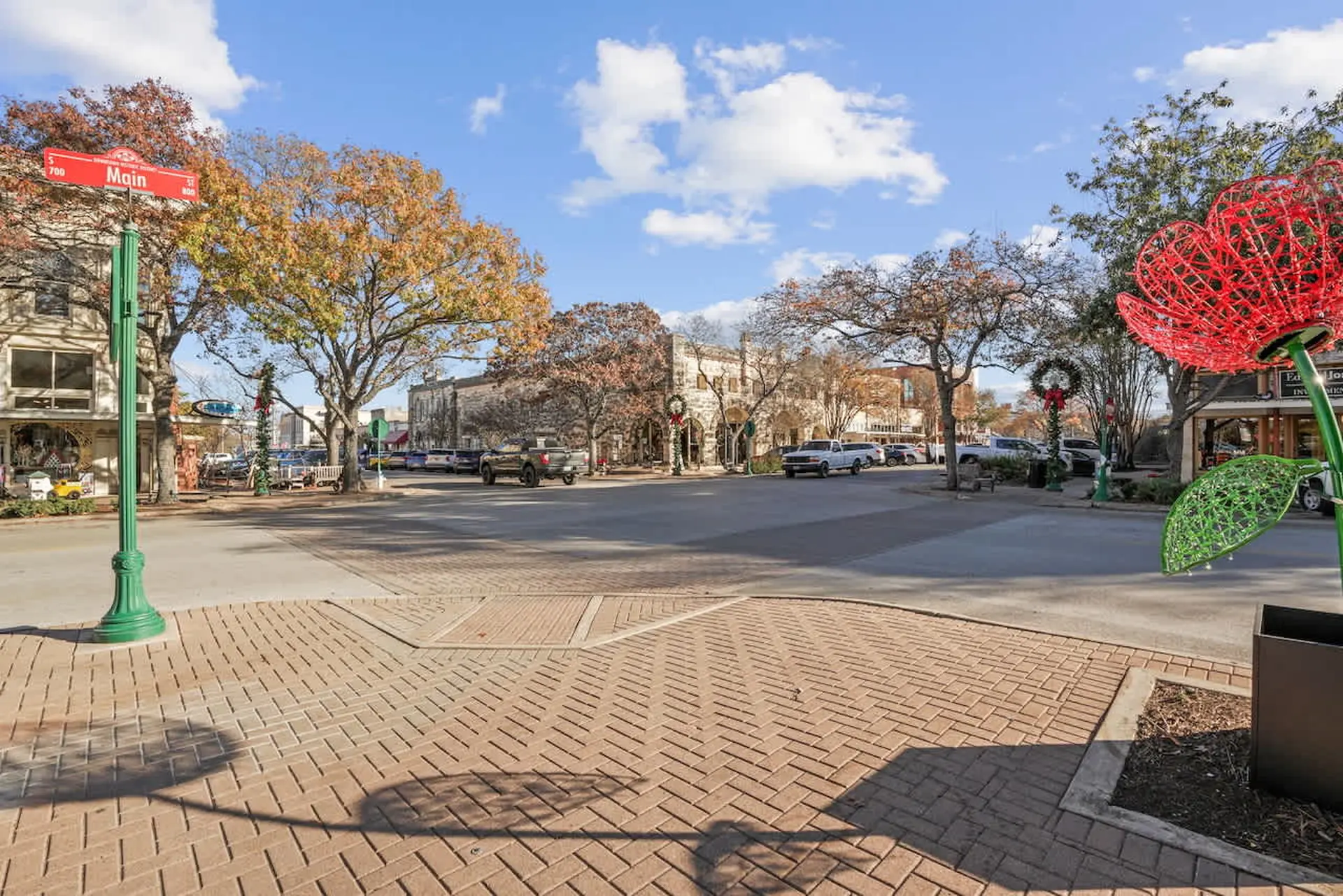 A street scene with a brick sidewalk, a large red flower sculpture, and buildings.