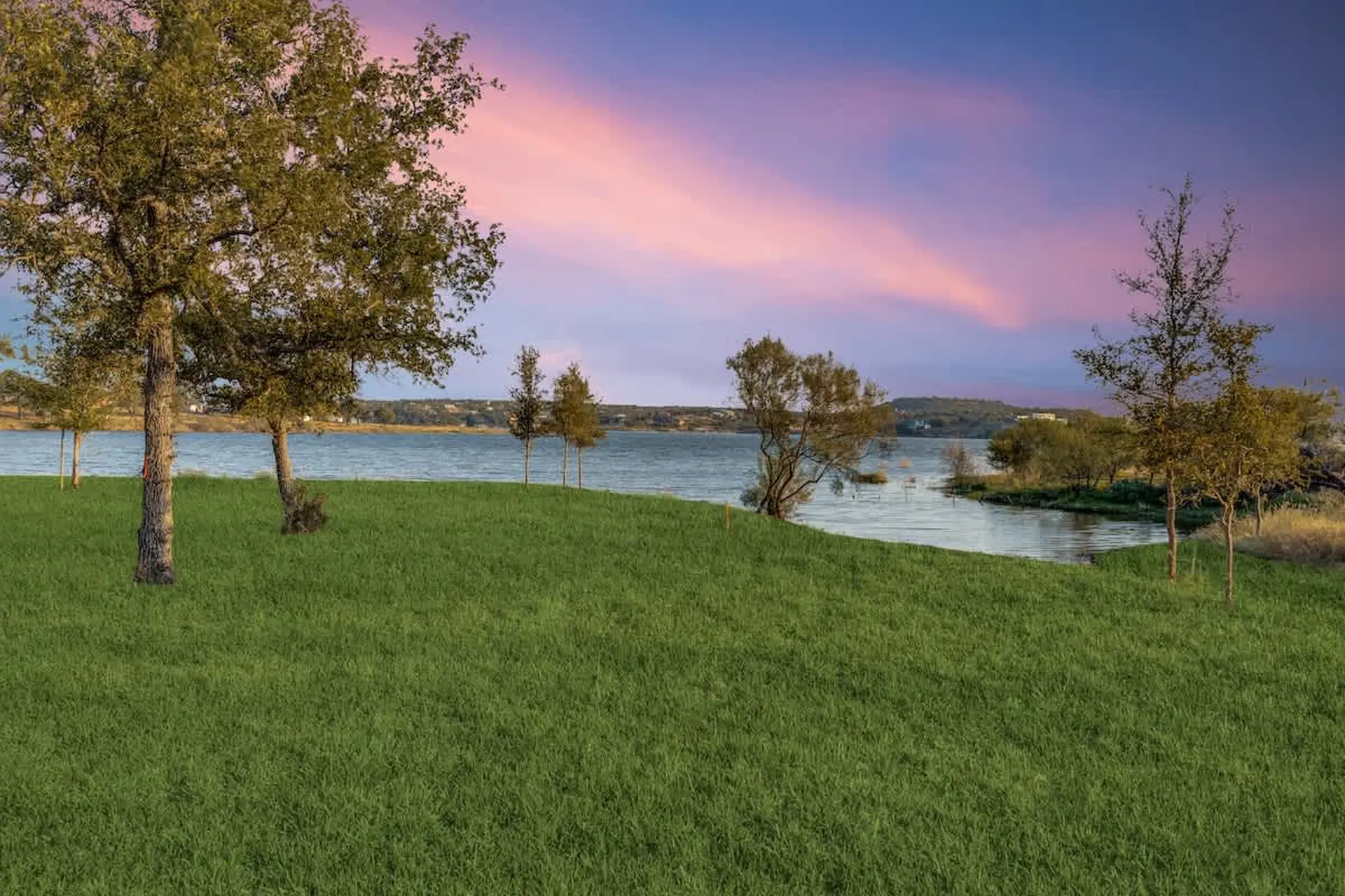 A serene lake at sunset with a gentle breeze rustling through trees and tall grass.