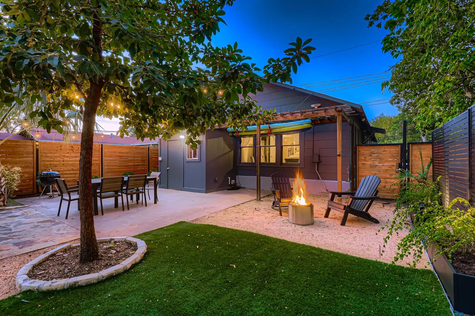 Backyard with a dining set, fire pit, Adirondack chairs, and a green lawn.