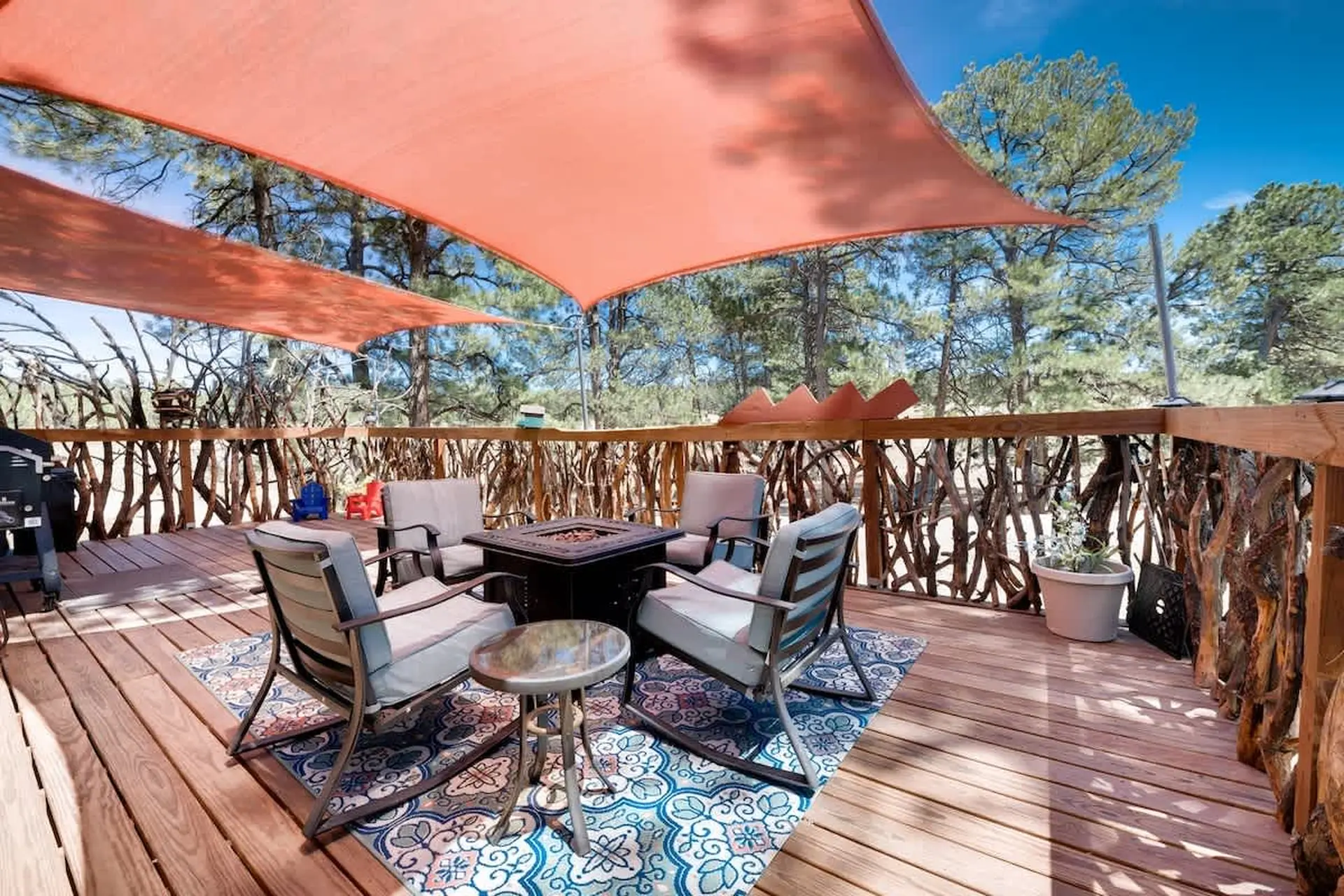 Outdoor deck with patio chairs around a fire pit, shaded by orange fabric sails.