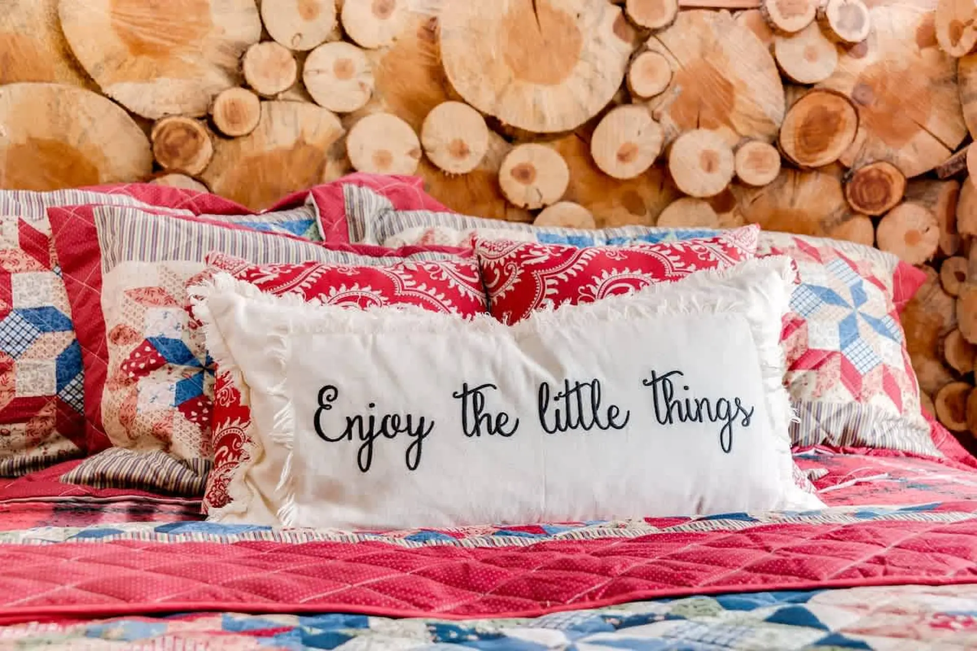 A close-up of a bed with a log headboard and a white pillow that reads "Enjoy the little things."