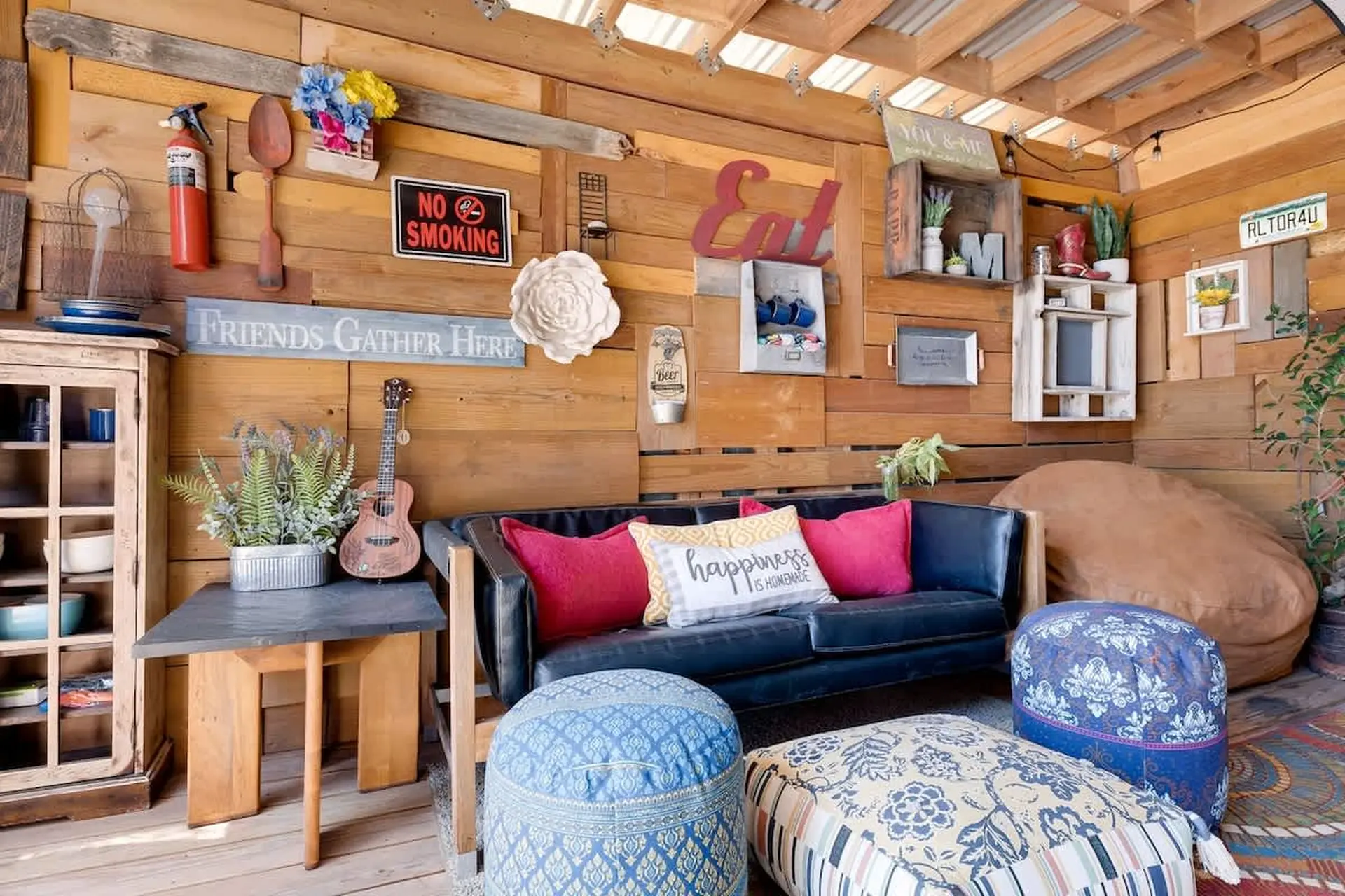 Cozy outdoor living room with a black sofa, colorful pillows, and patterned poufs.