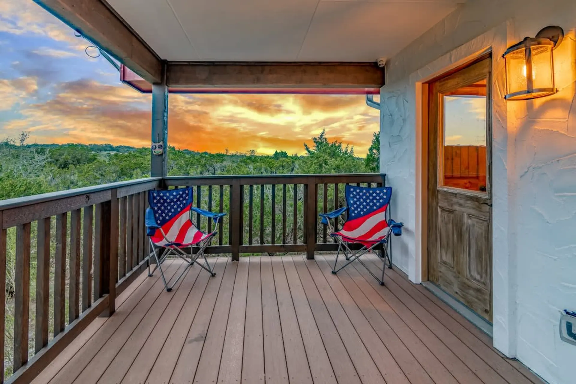 Two chairs with American flag designs on a wooden deck overlooking a sunset.