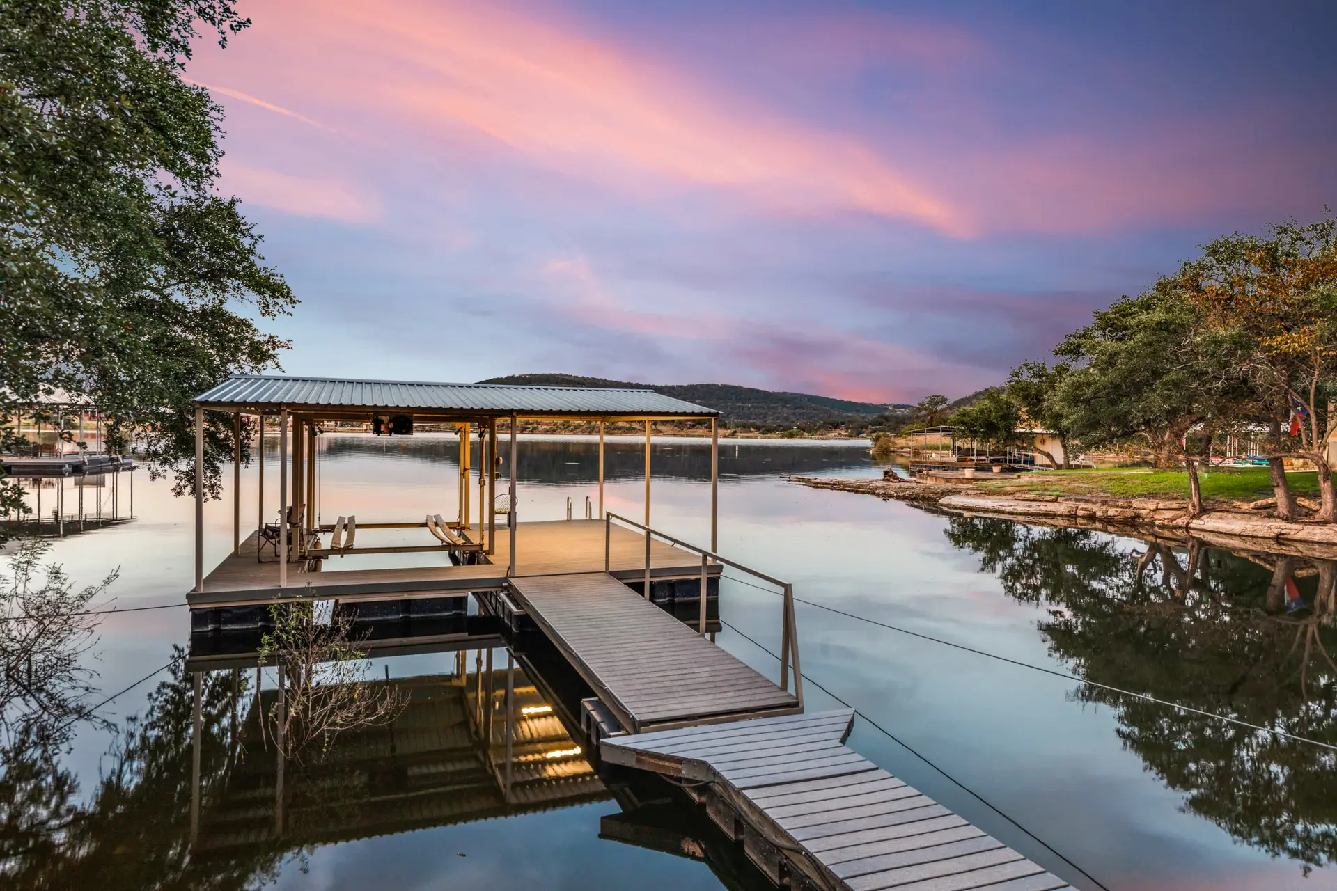 A serene lake at sunset with a boat dock and trees reflecting in the water.