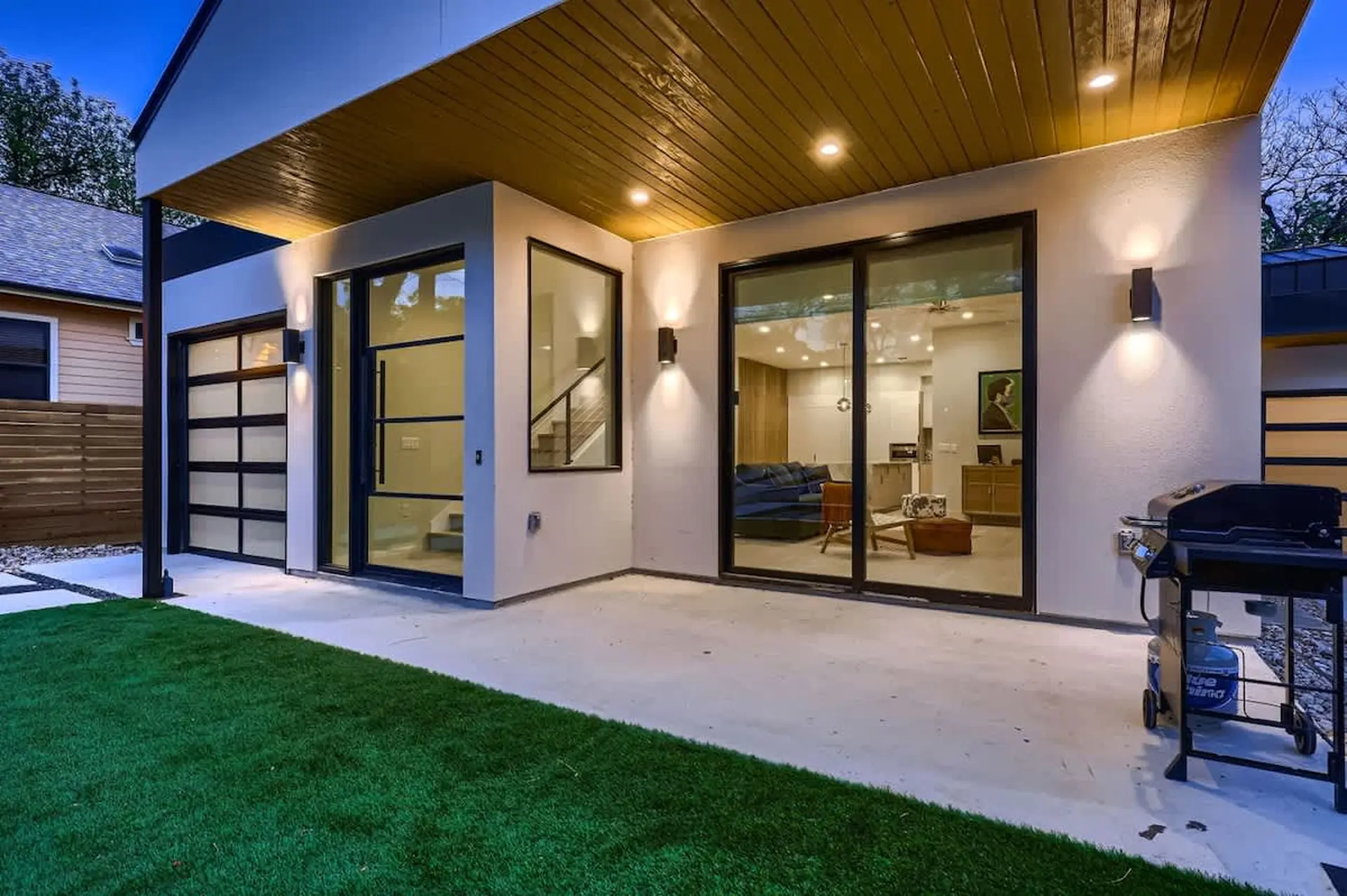 Modern home with glass garage, large sliding doors, patio, and BBQ.