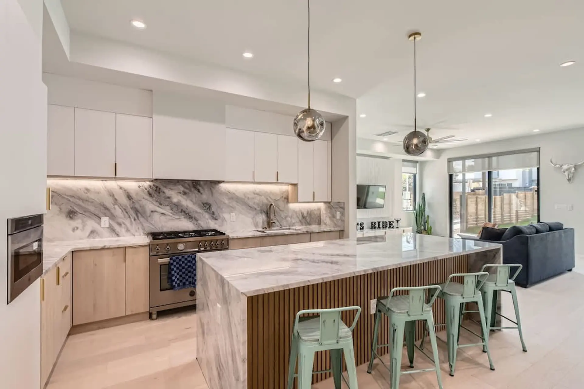 Modern kitchen with marble island, light wood cabinets, and bar stools.
