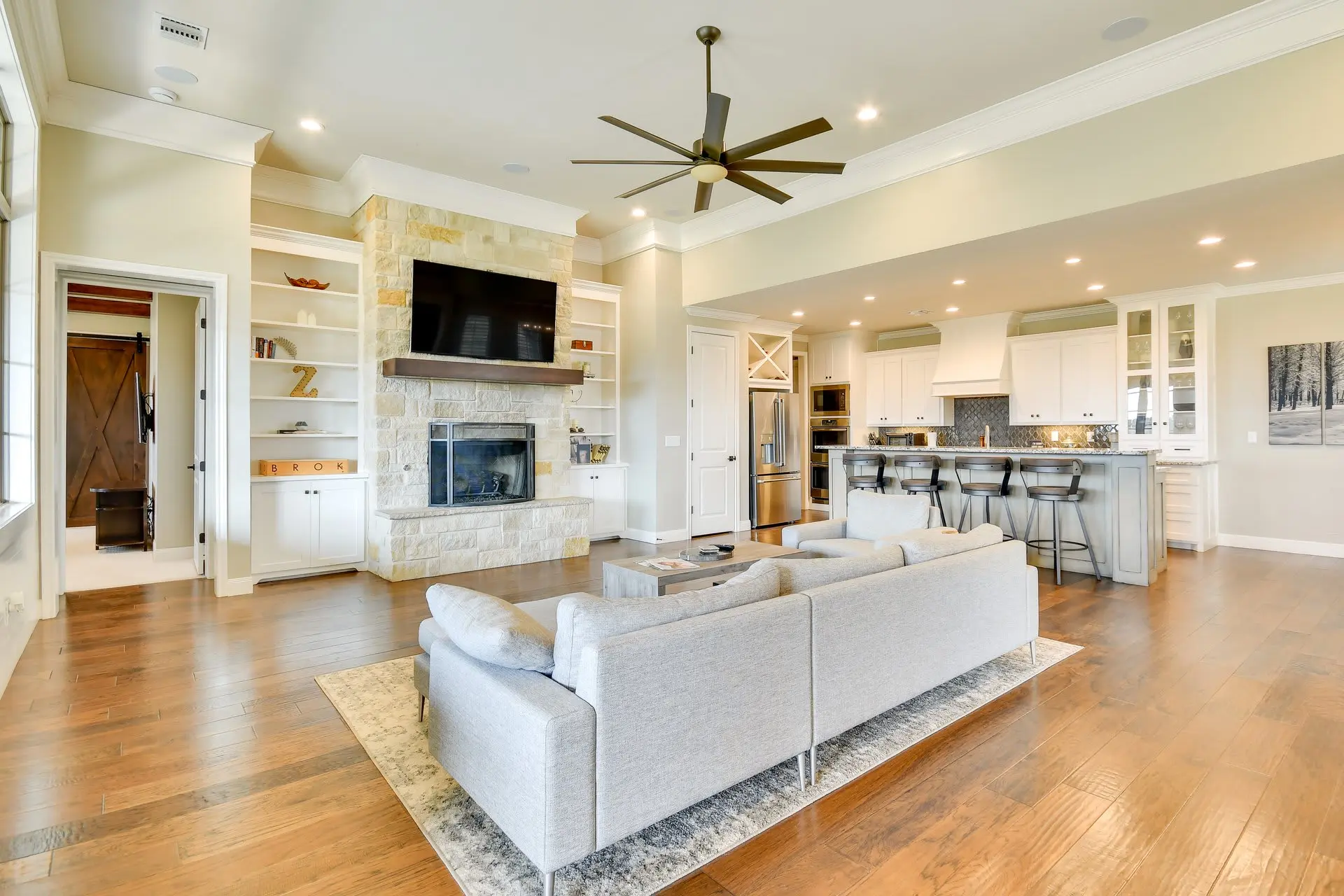 A bright, open-concept living and kitchen area with a stone fireplace and a large sectional sofa.