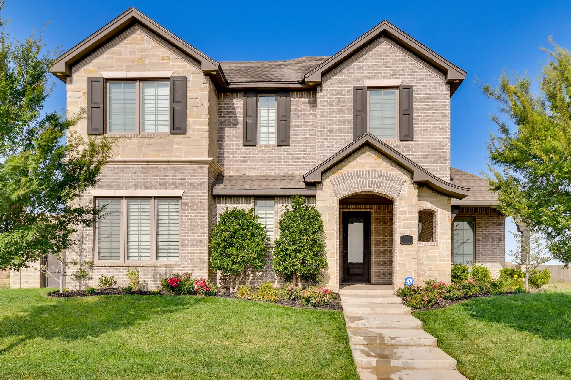 A front view of a large, two-story brick house with a covered entryway and green lawn.