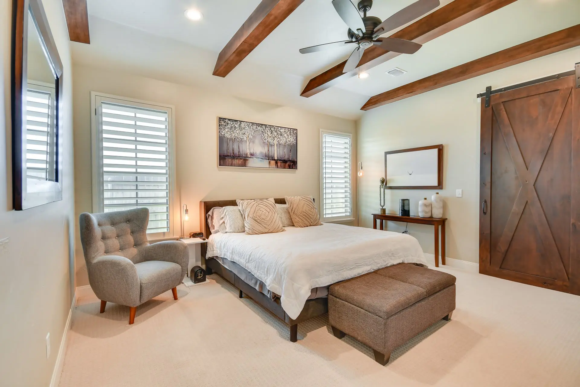 A bedroom with a ceiling fan, wooden beams, and a sliding barn door.