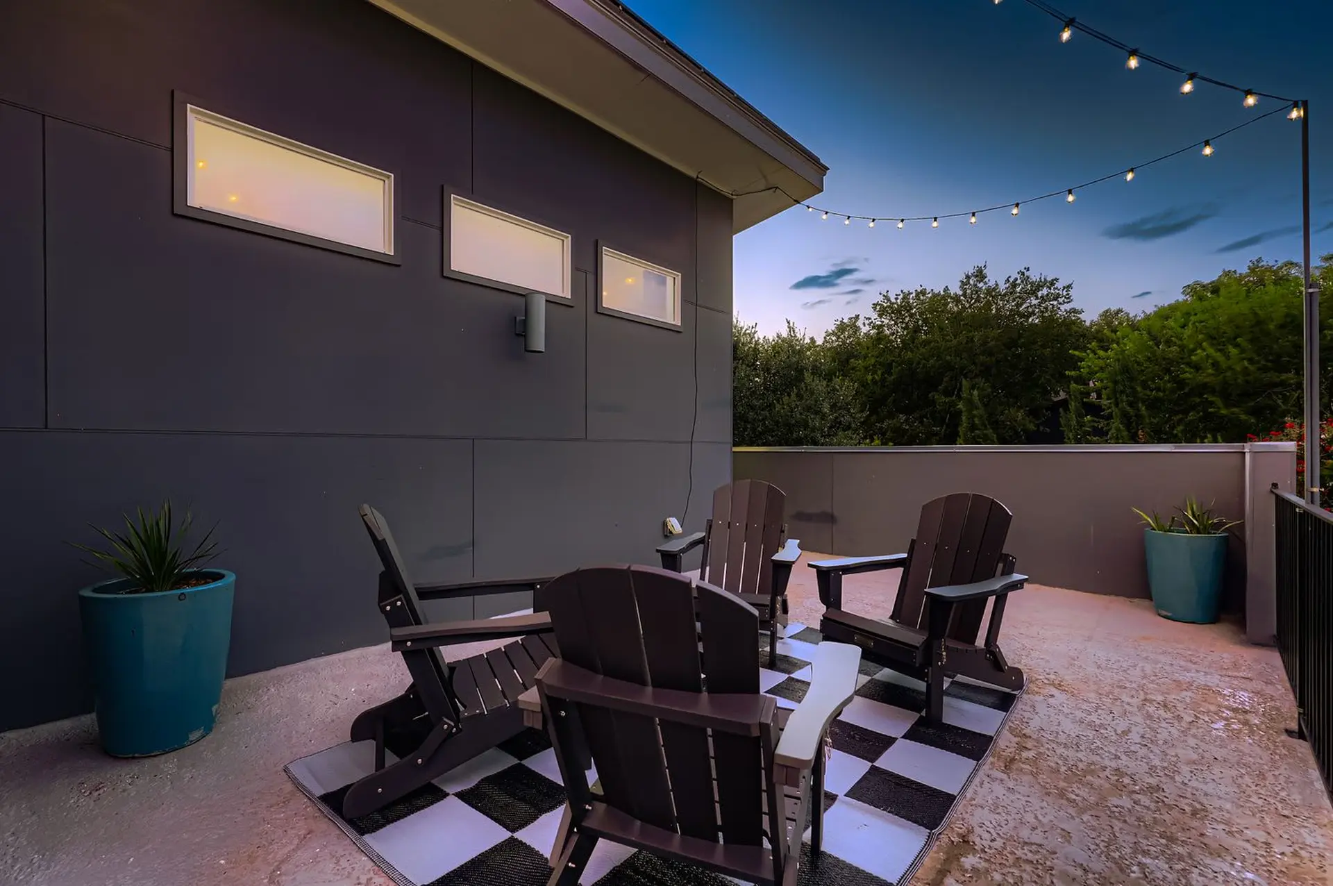 Outdoor patio with dark Adirondack chairs arranged on a checkered rug.