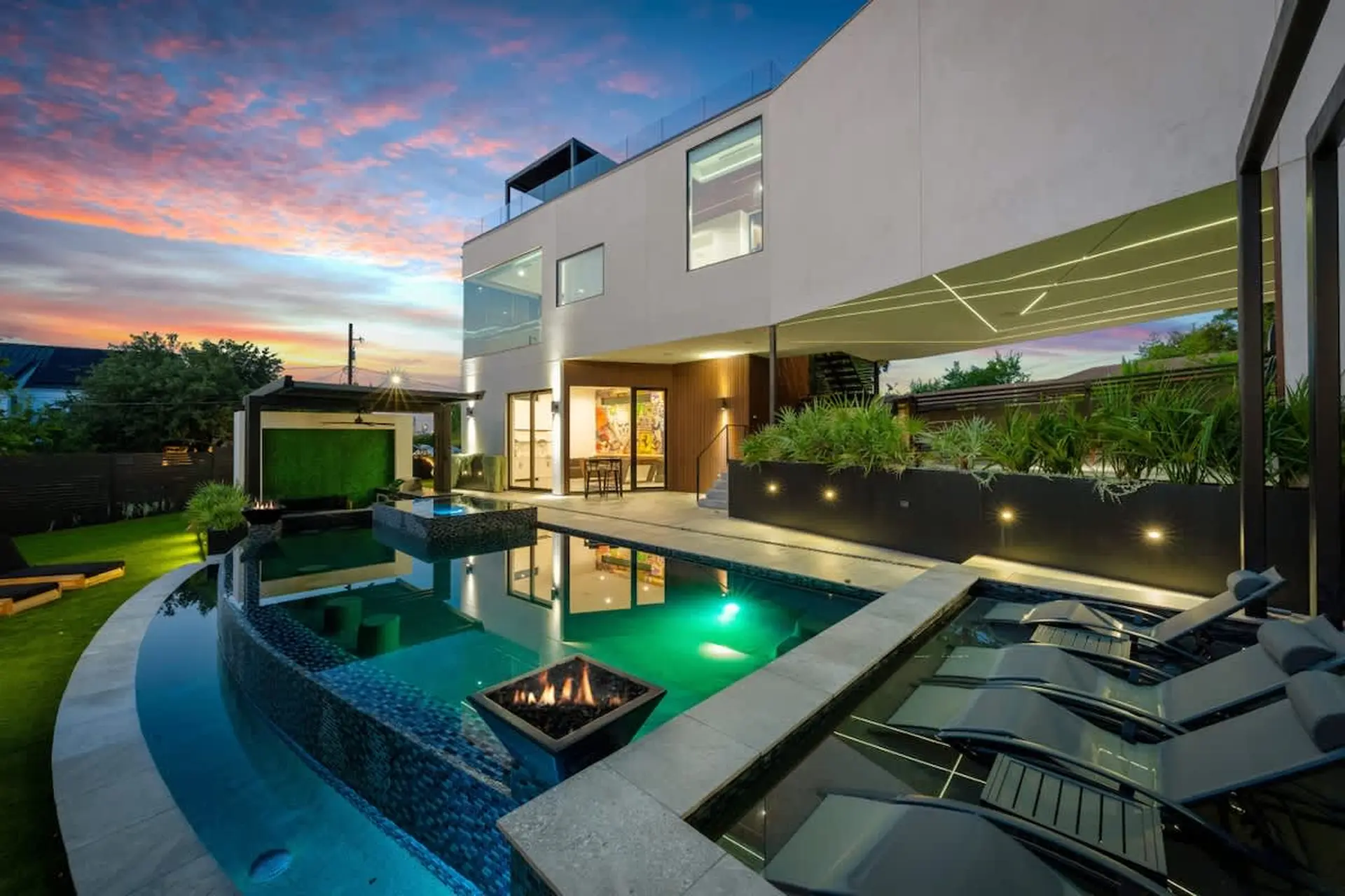 Modern house with a swimming pool and lounge chairs at sunset.