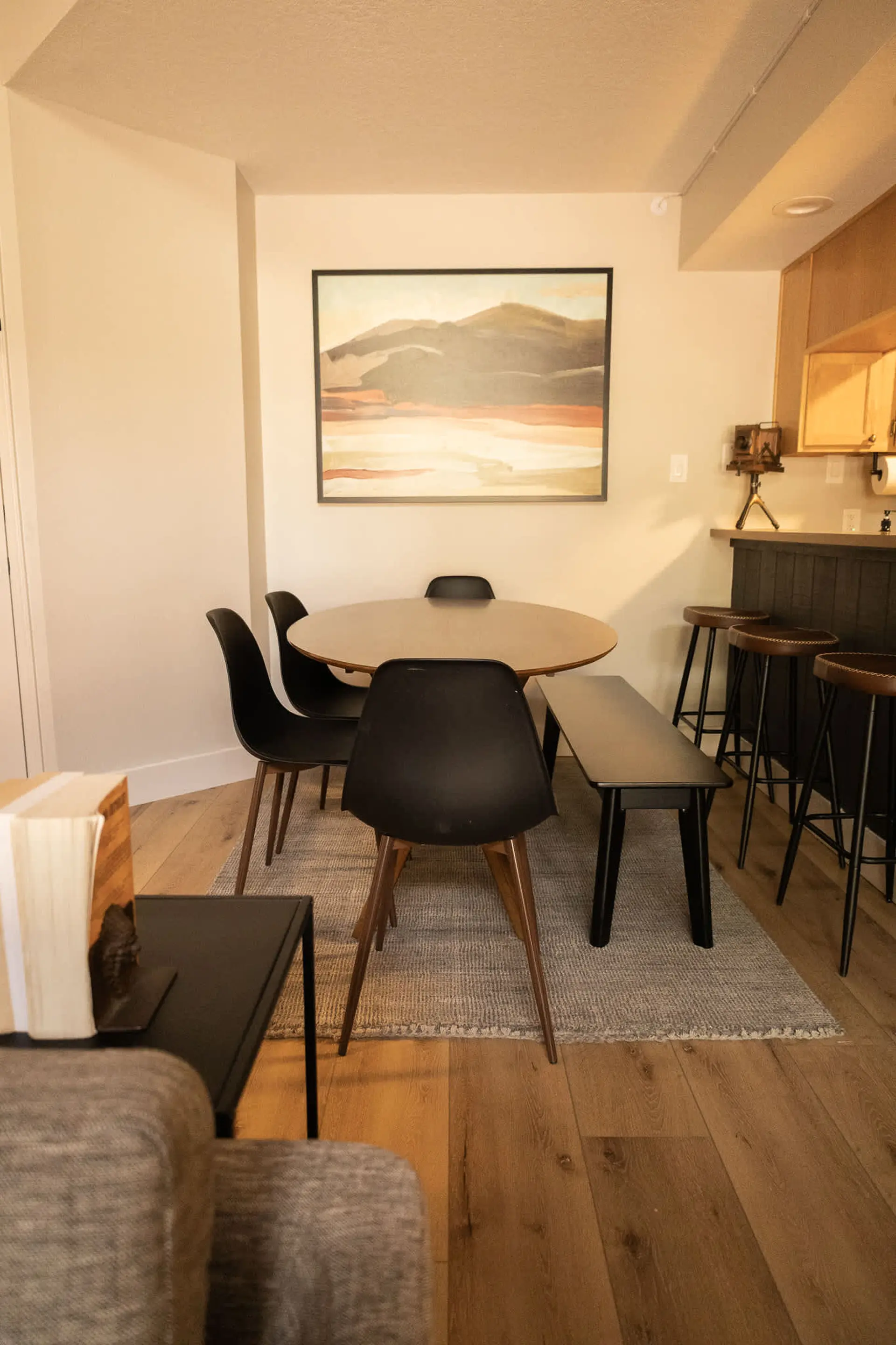 A round dining table with black chairs and a bench is on a rug.