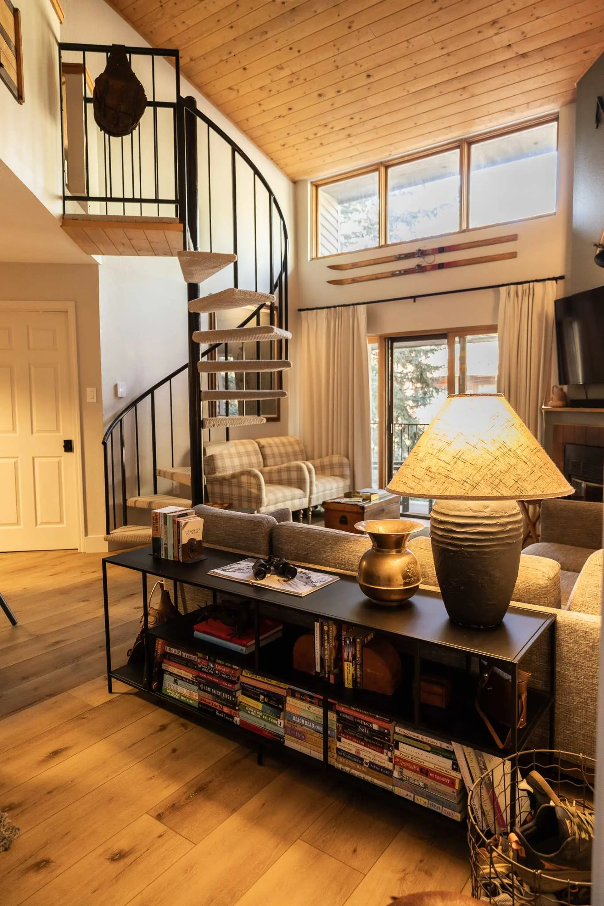A living room with a spiral staircase, plaid armchairs, and a large shelf filled with books.