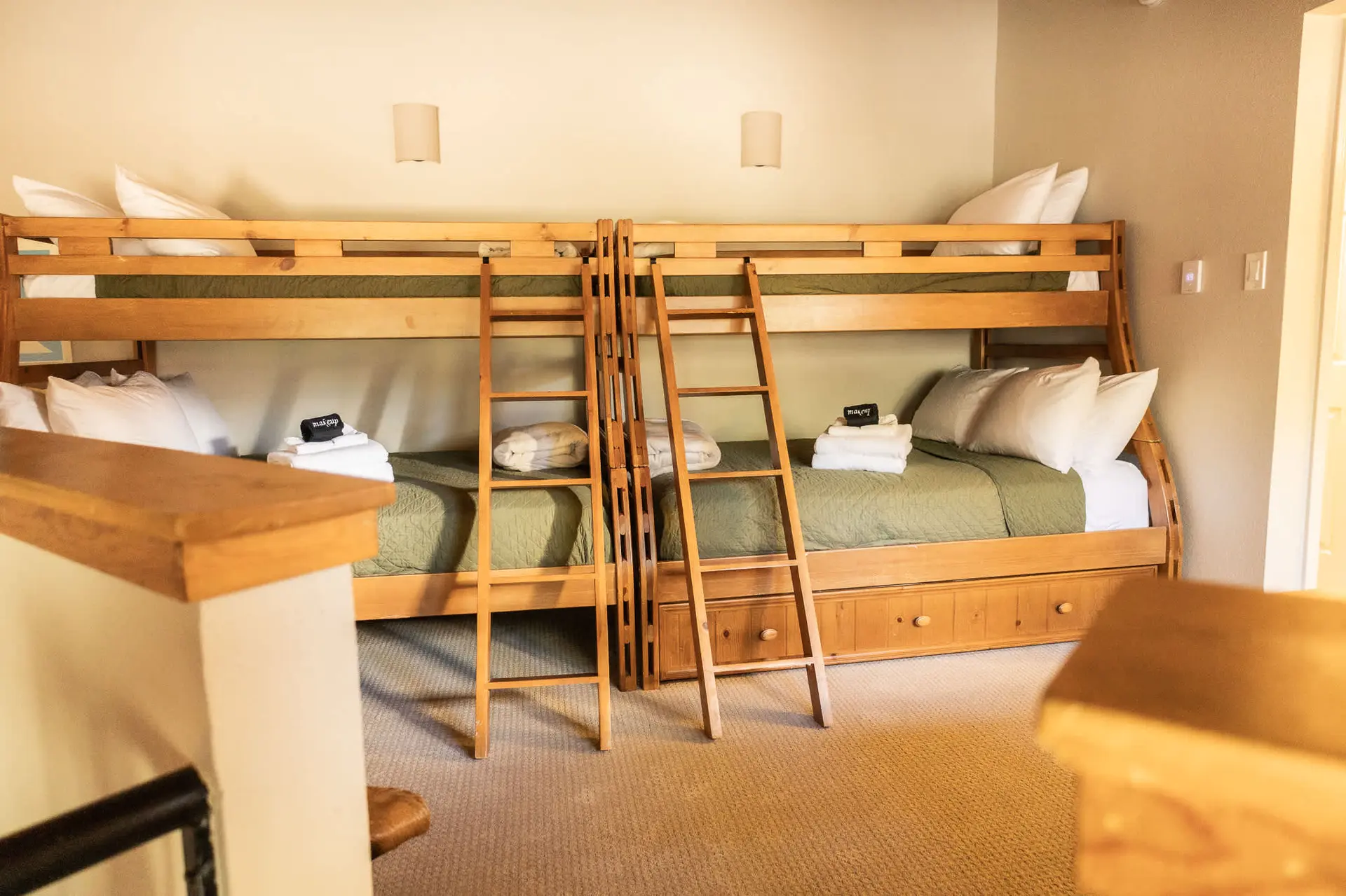 Bunk beds with green bedding and white pillows are neatly made with towels and a makeup bag.