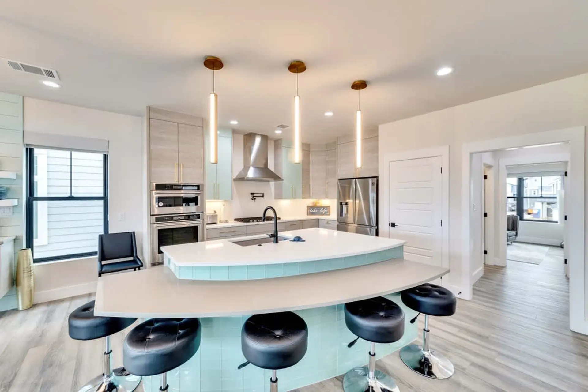 Modern kitchen with island, bar stools, stainless steel appliances, and pendant lighting.