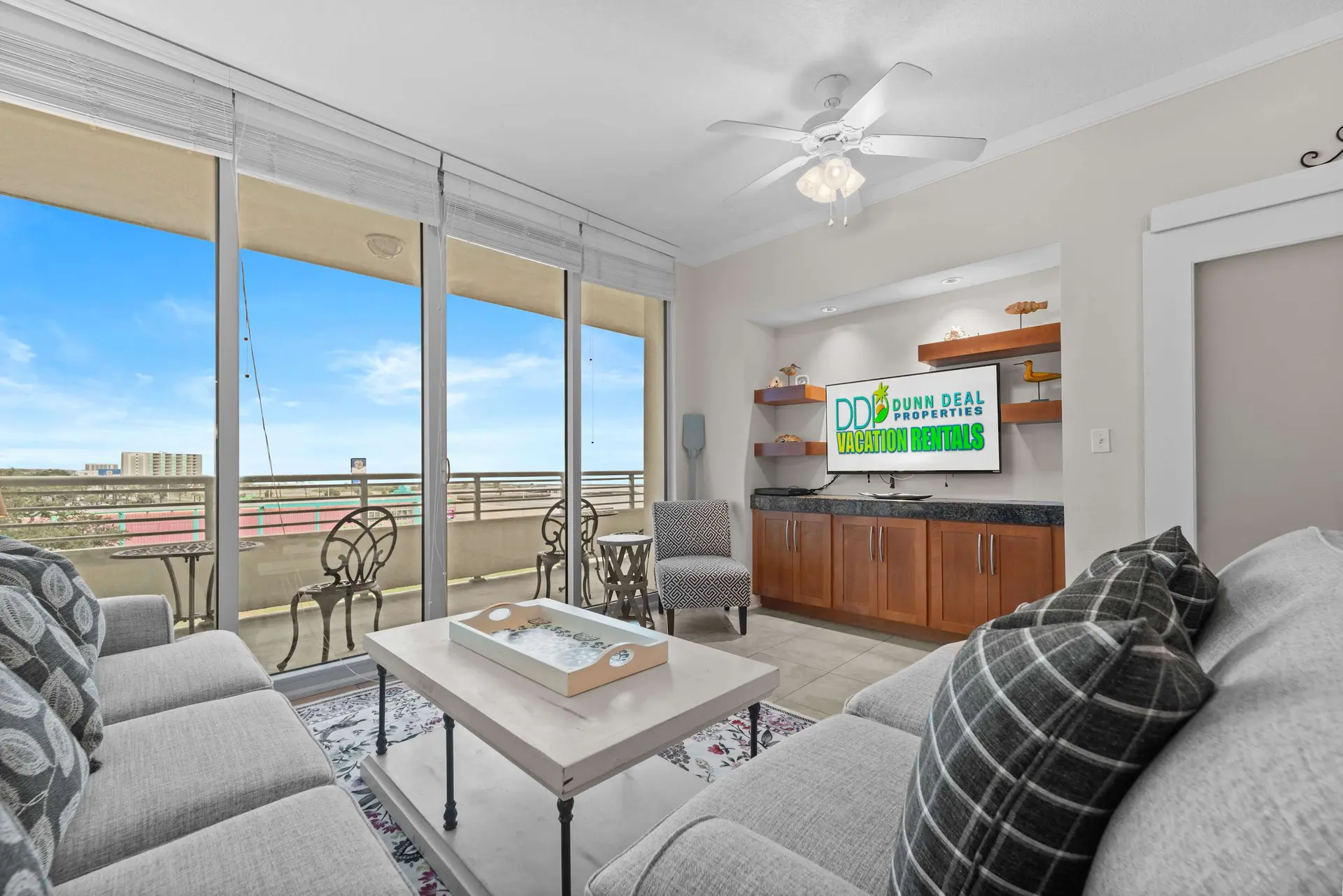 Living room with a sectional sofa facing a TV and a large window with a view of a balcony.