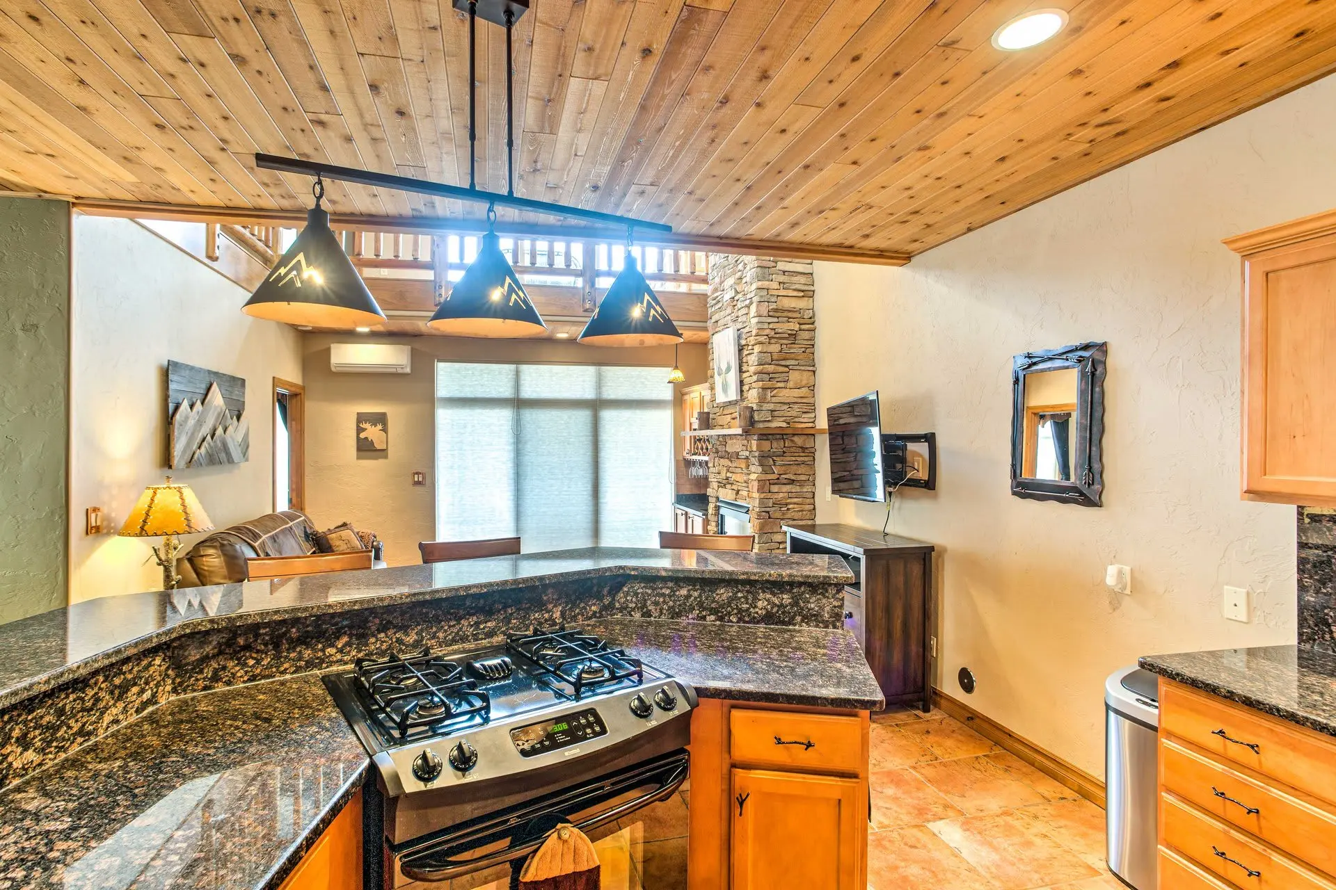 A kitchen with a granite countertop, gas stove, and wooden ceiling.