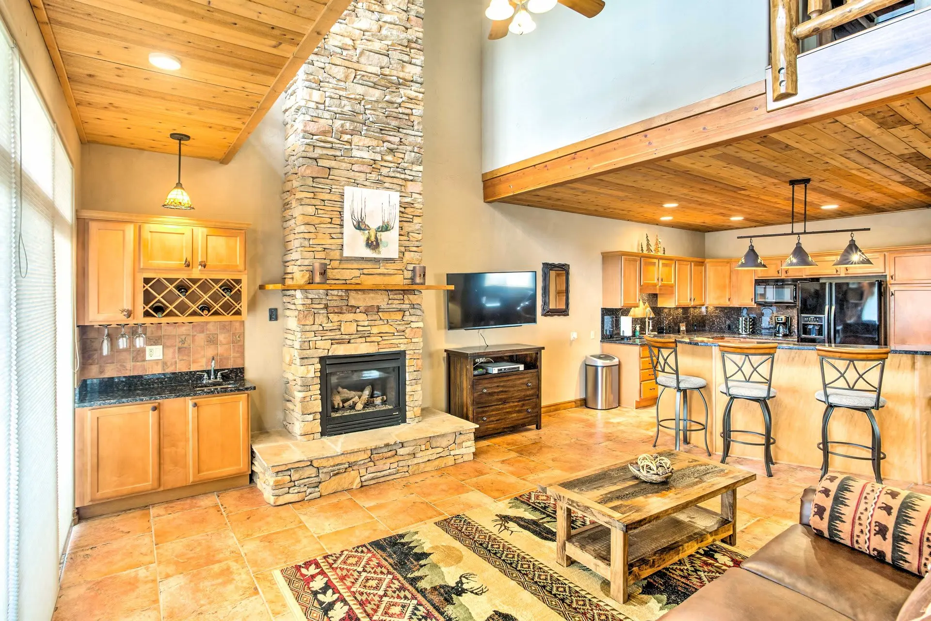 A rustic living room with a stone fireplace, wood beams, and kitchen island.