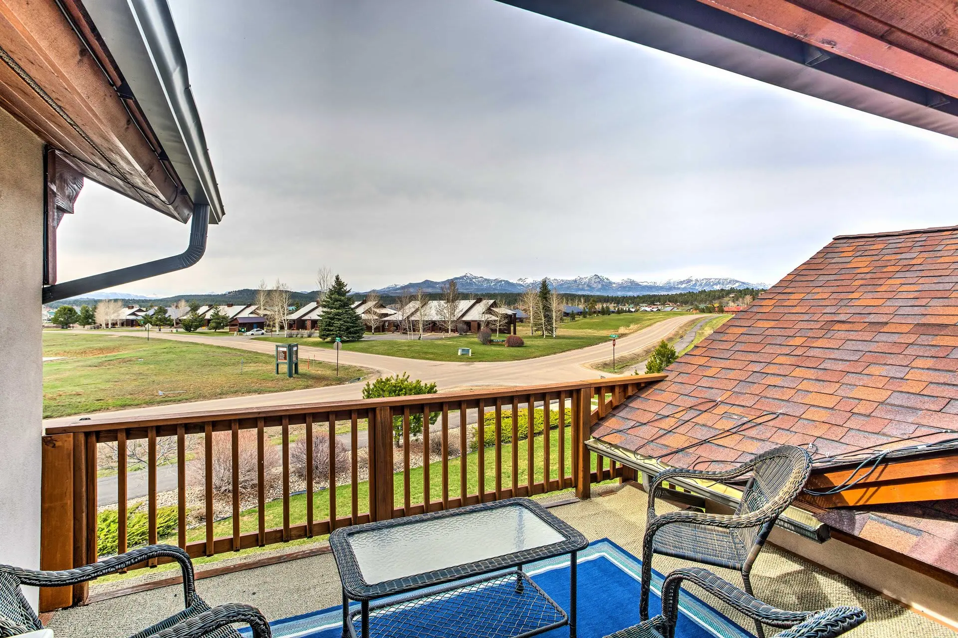 Balcony with wicker chairs and table overlooking a suburban neighborhood with mountains in the dista