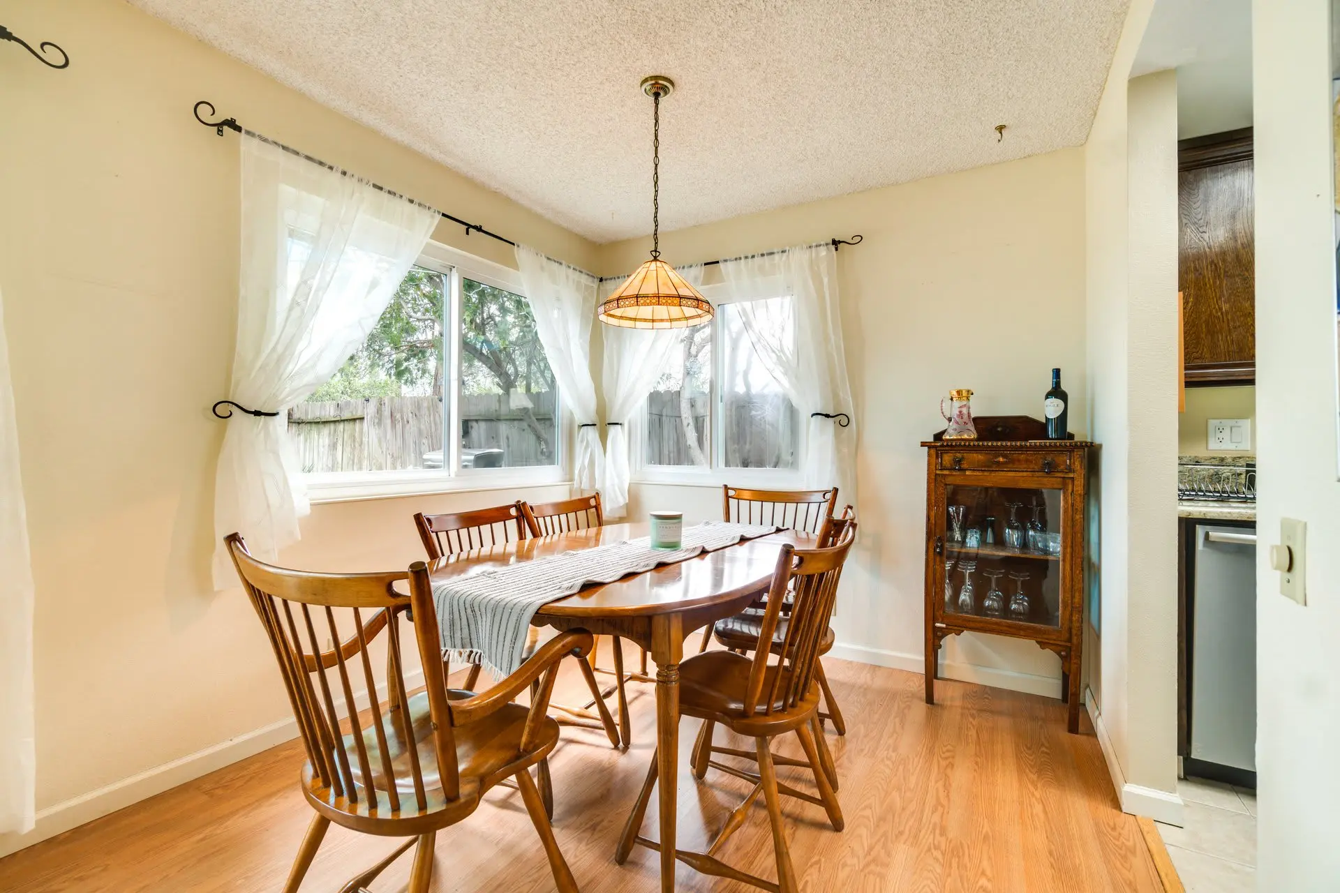 A dining room table with chairs, a hutch, and a window with sheer curtains.