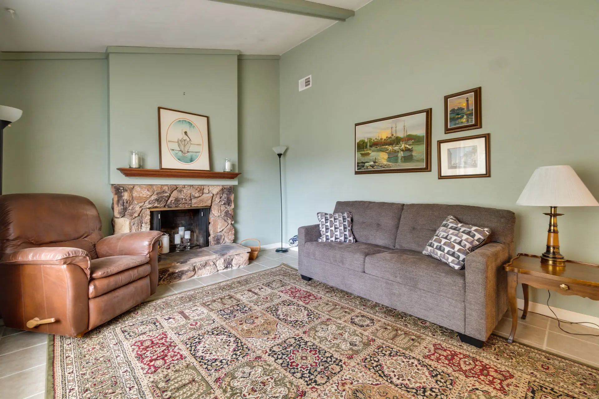 A cozy living room with a leather recliner, a couch, fireplace, and artwork.