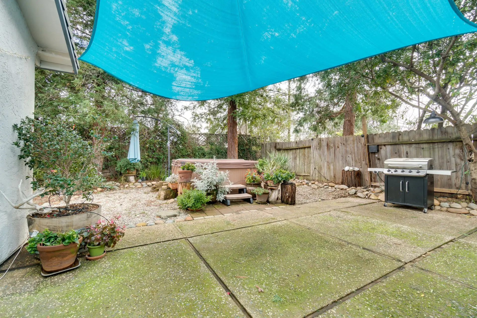 A backyard patio features a hot tub, a grill, and concrete flooring.